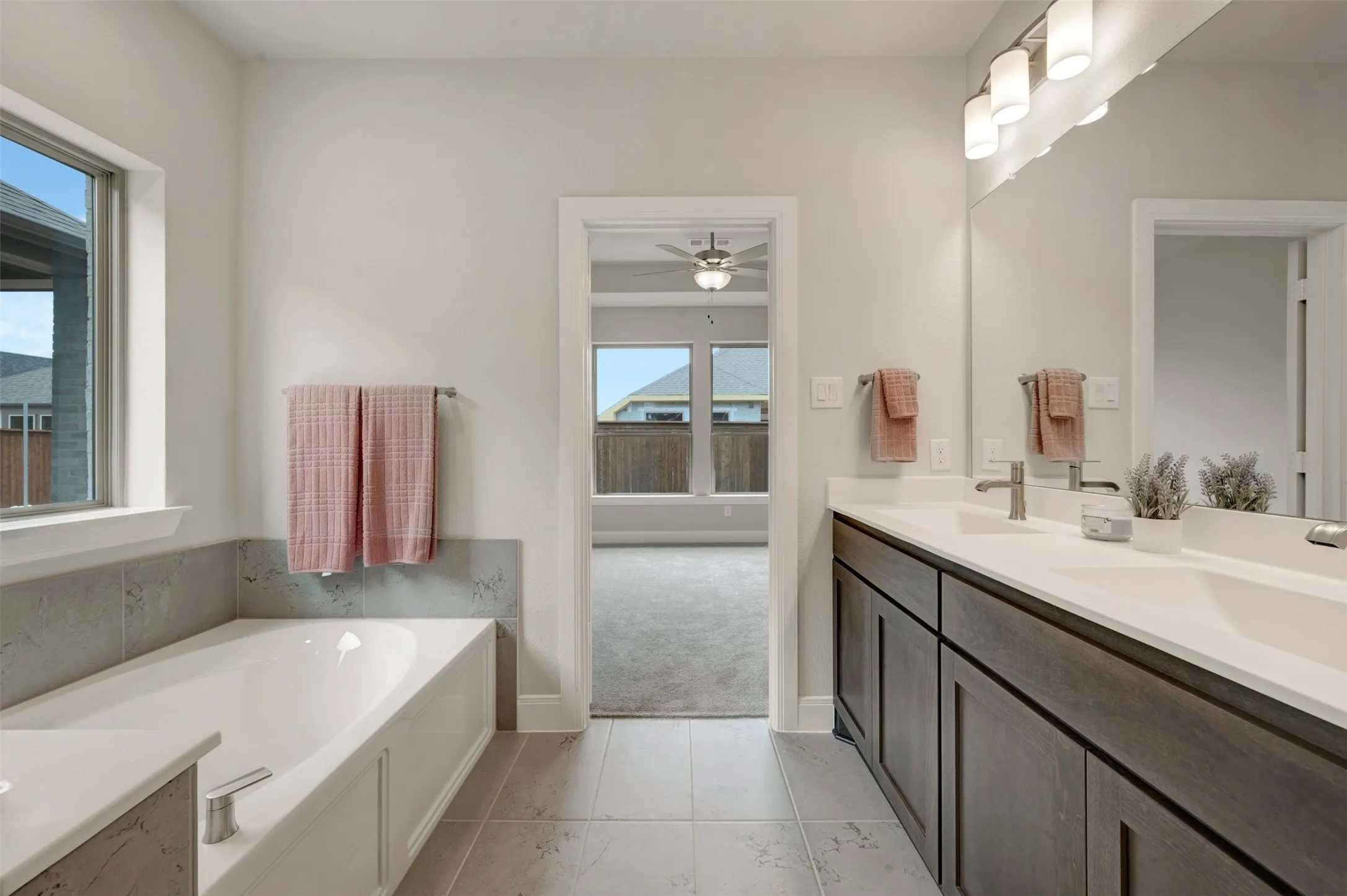 Bathroom featuring a built-in soaking tub with a tiled surround, a dual vanity with a white countertop and dark wood-finish cabinetry, and tiled flooring