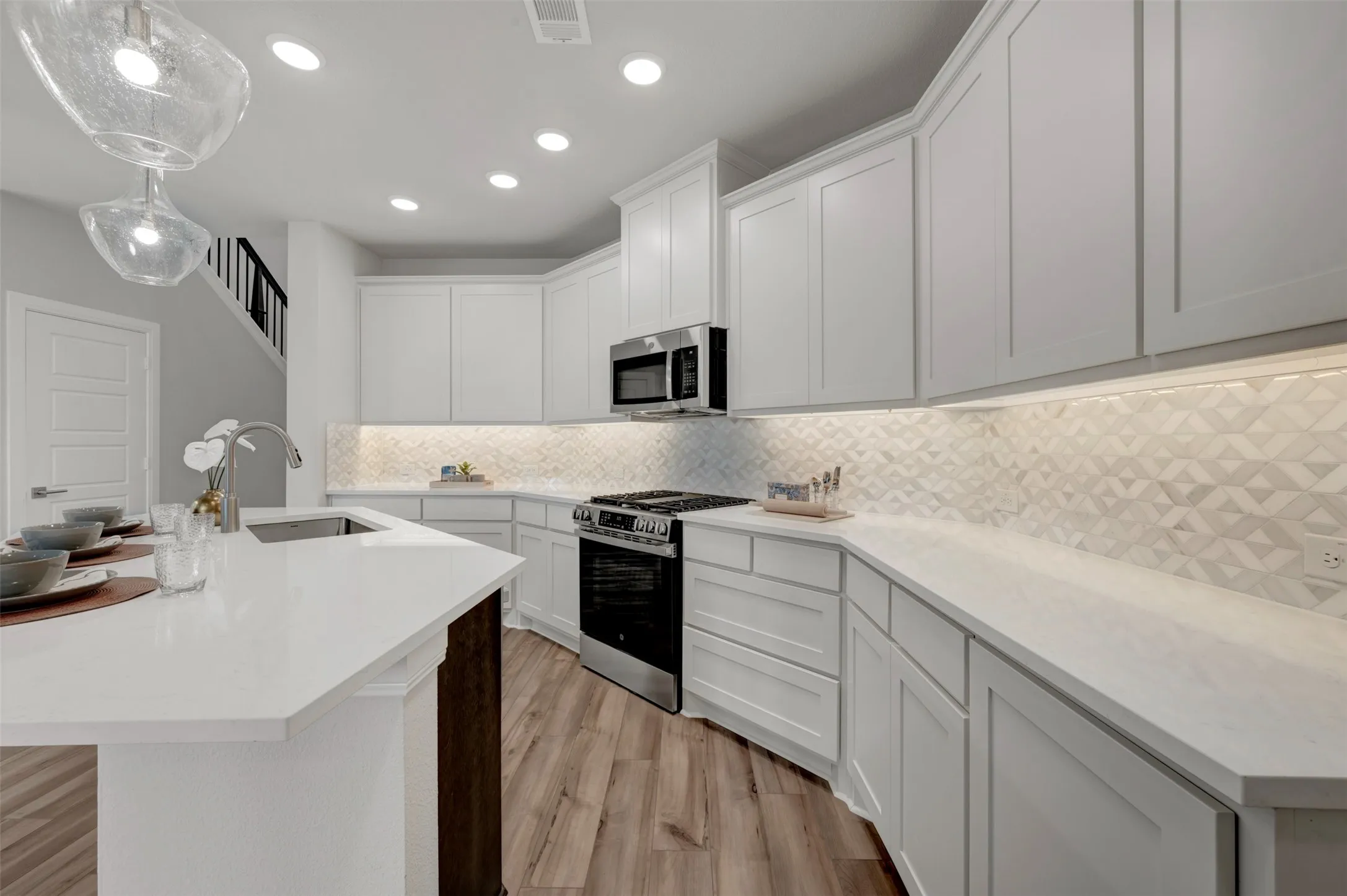 Spacious kitchen featuring white cabinetry, light-toned countertops, and a decorative tile backsplash with under-cabinet lighting