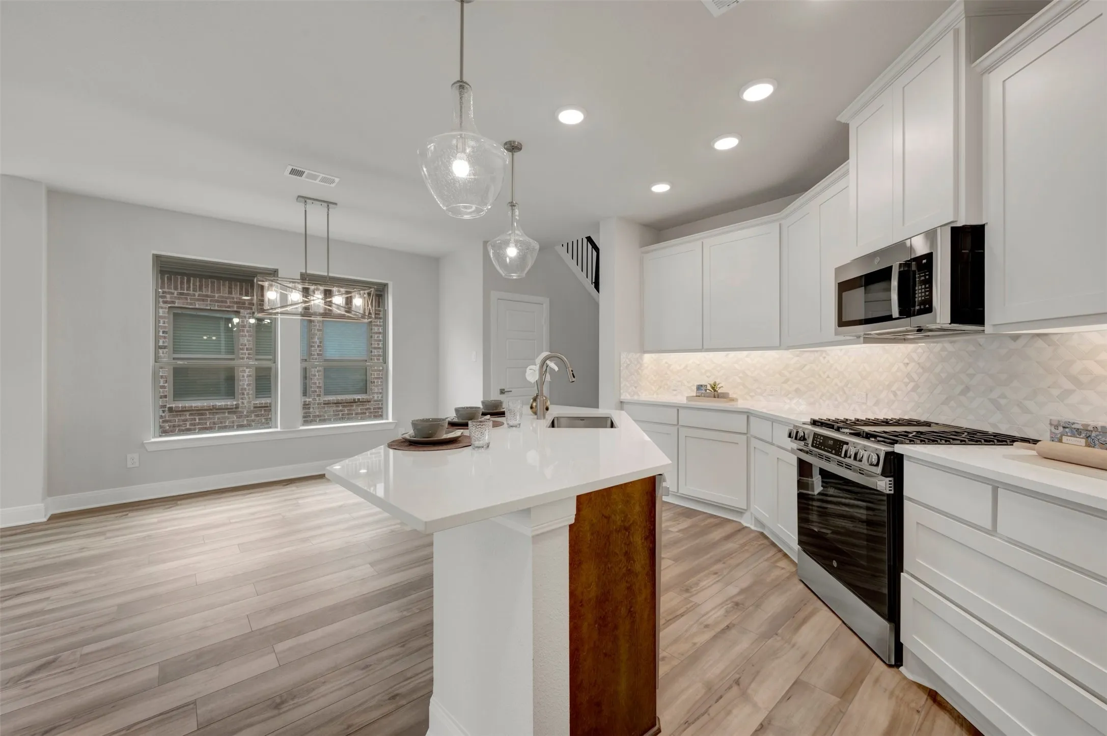 Contemporary kitchen featuring white cabinetry, stainless steel appliances, a white tile backsplash, and a central island with a sink and seating area