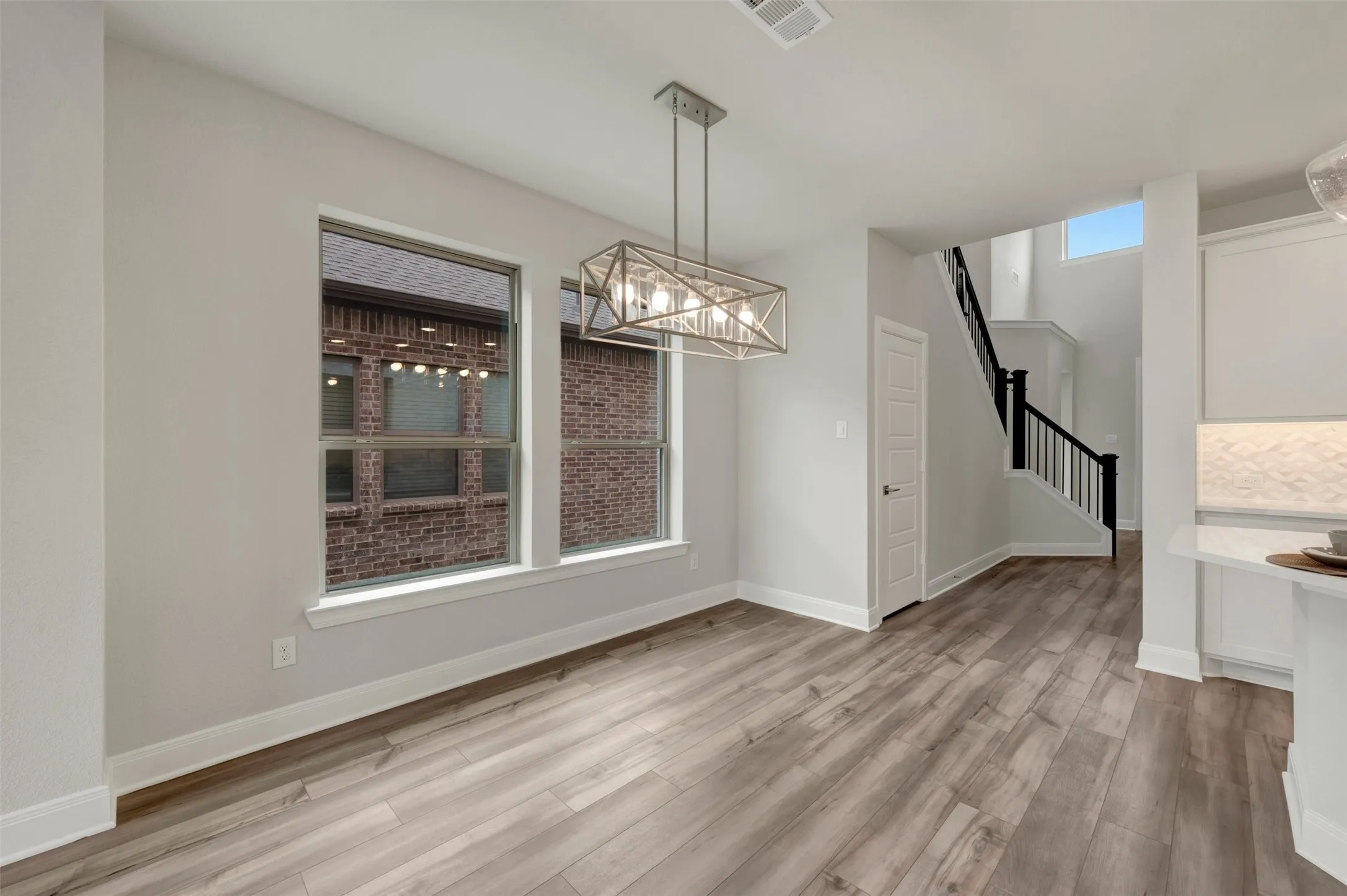 Open concept dining area featuring wood-finish flooring, a modern linear chandelier, and two large windows