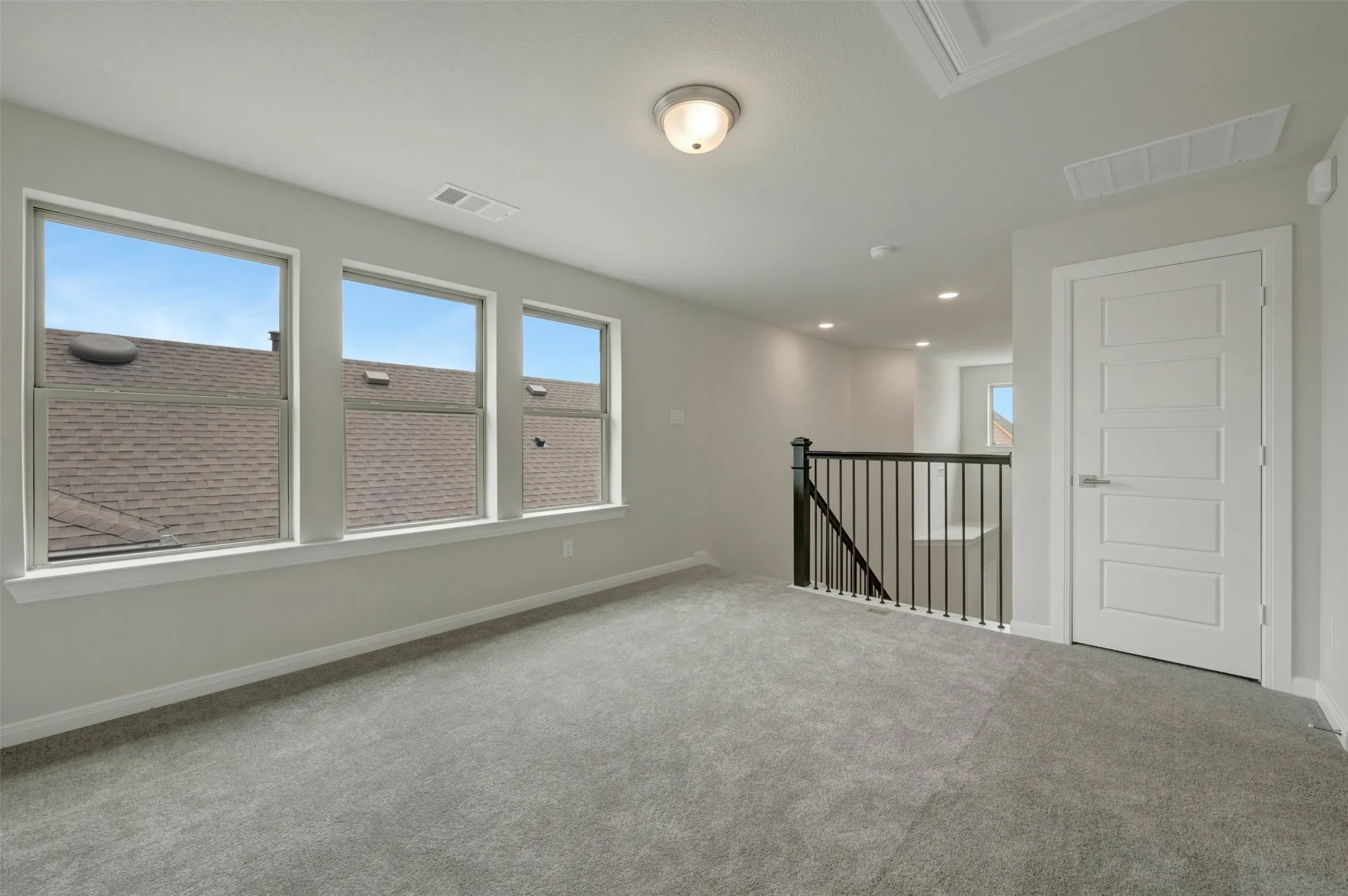 Carpeted upper-level space featuring three windows, a white five-panel door, and a black wrought iron staircase railing