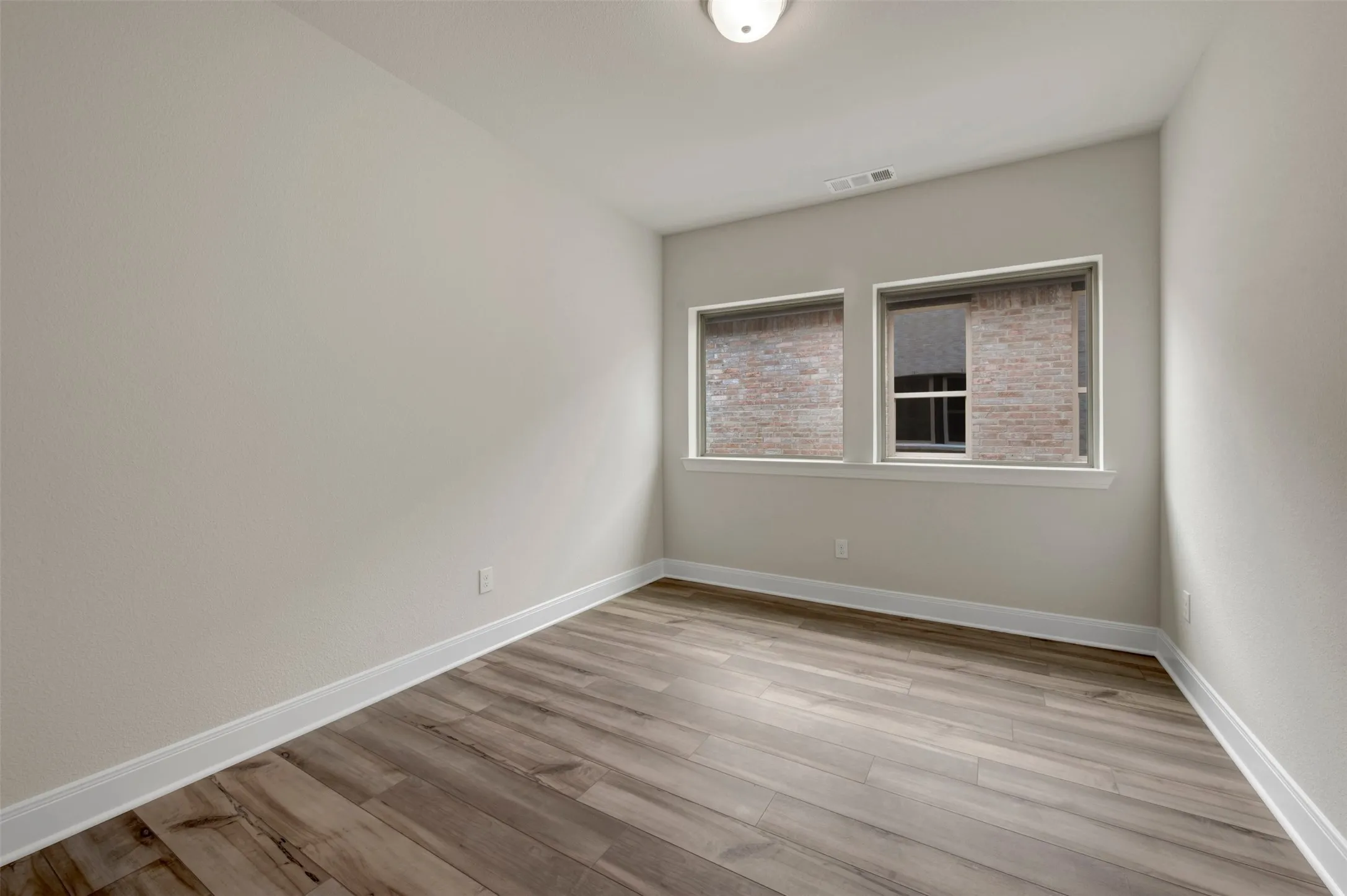 Neutral wall paint with white trim, wood-finish flooring, and two rectangular windows