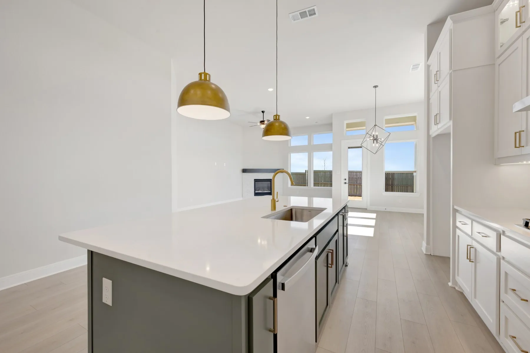 Two tone kitchen with dual tone cabinets, an island with sink, light wood-style flooring, a glass covered fireplace, and stainless steel dishwasher