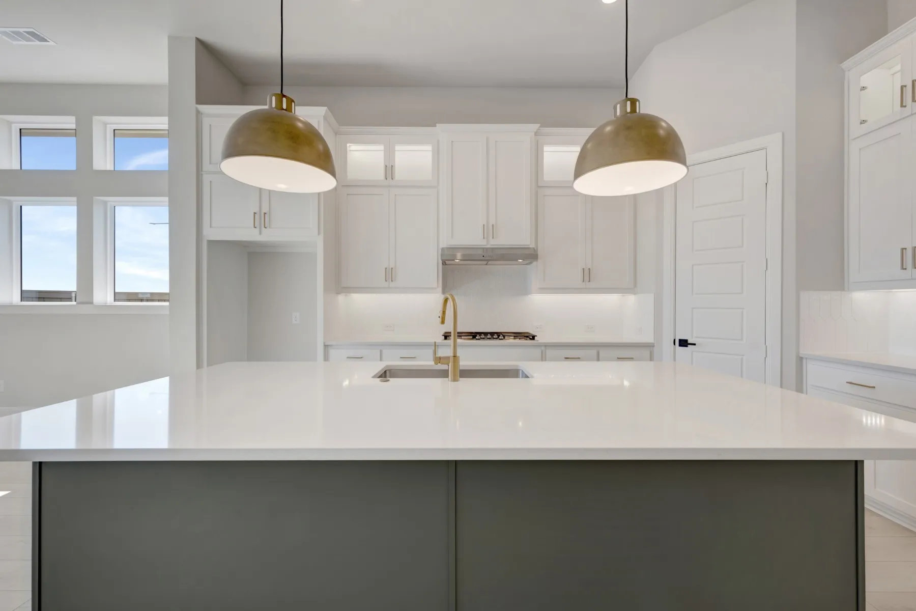 Two tone kitchen featuring dual tone cabinetry, glass fronted cabinets, pendant lighting, light stone countertops, and a center island with sink