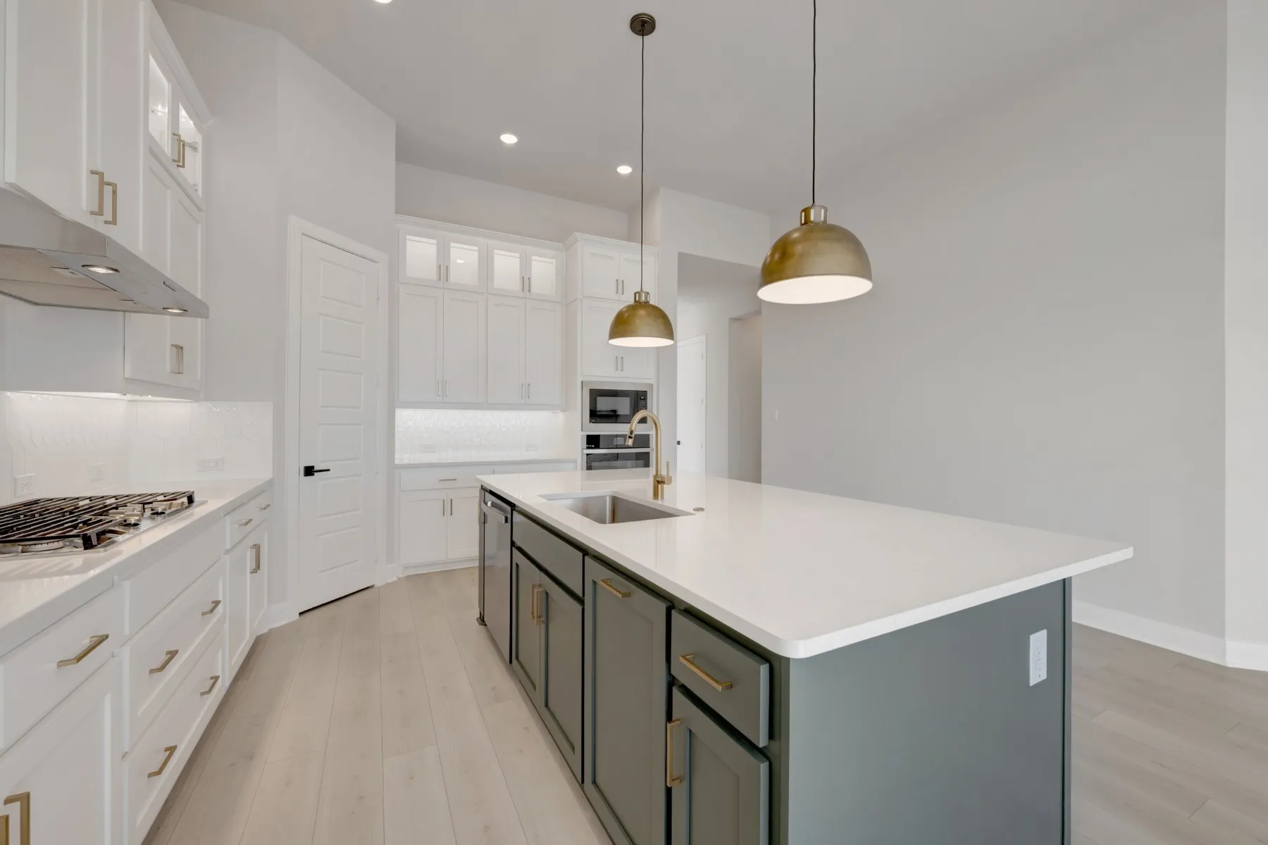Kitchen featuring two tone cabinets, glass fronted cabinets, pendant lighting, light wood finished floors, and a kitchen island with sink