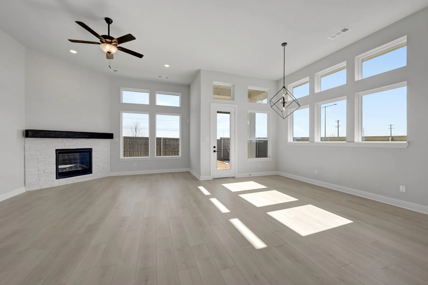 Unfurnished living room featuring ceiling fan, a fireplace, suspended lighting, and light wood-style flooring