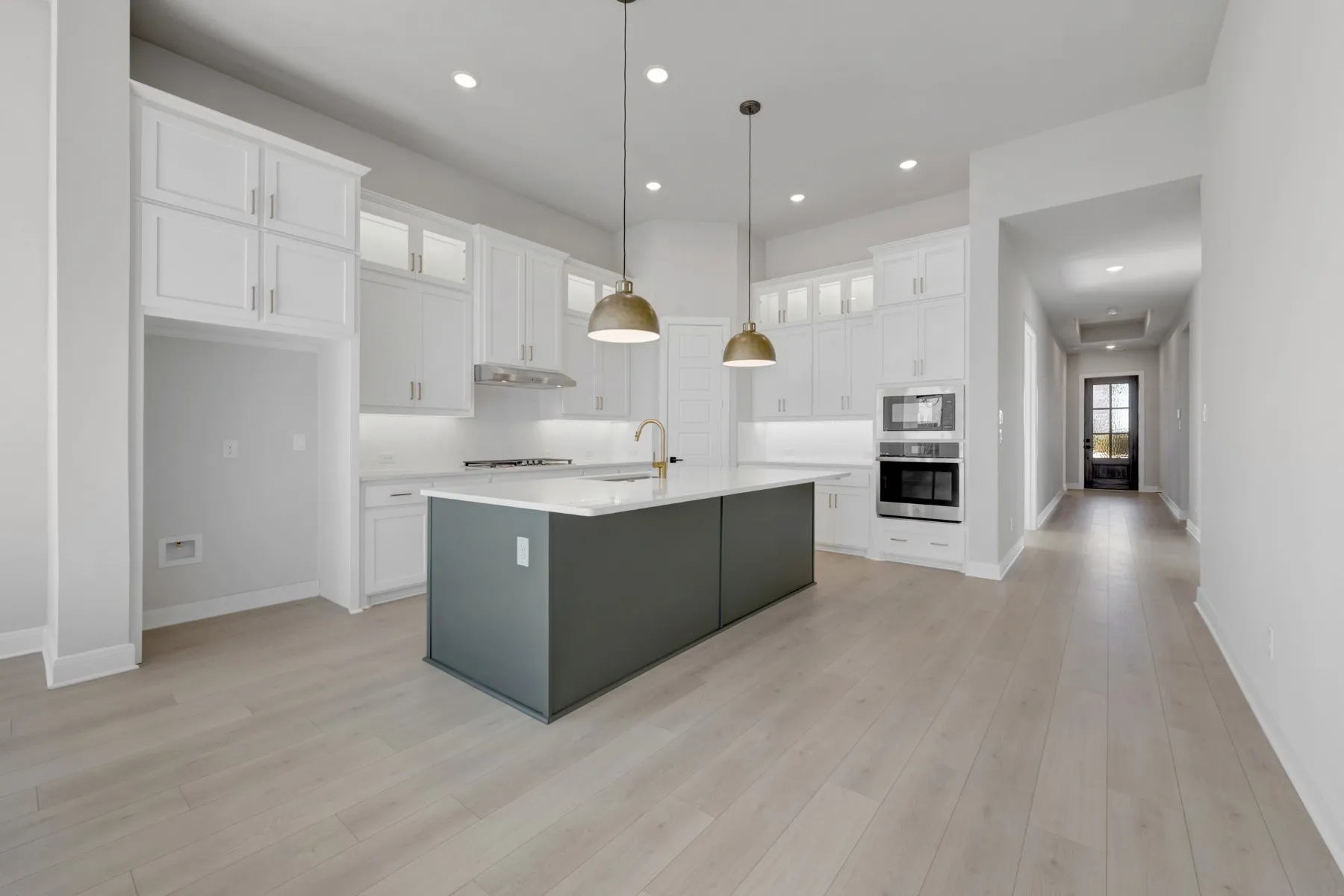 Dual tone kitchen featuring glass fronted cabinets, an island with sink, stainless steel appliances, pendant lighting, and two tone cabinetry