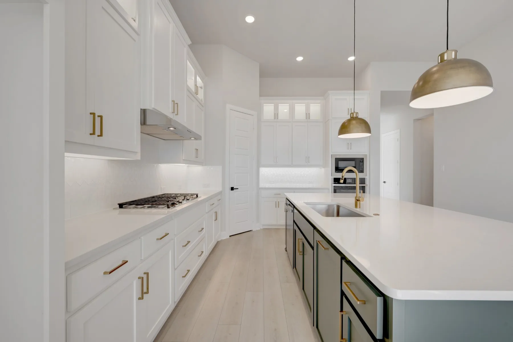 Two tone kitchen with two tone color scheme, a kitchen island with sink, glass insert cabinets, pendant lighting, and light wood-style floors