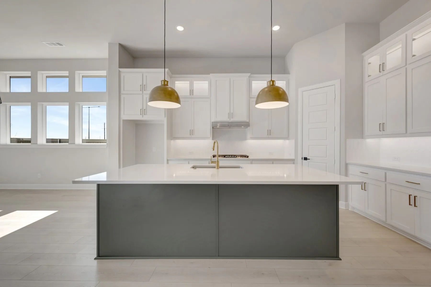 Kitchen with light wood-style flooring, pendant lighting, dual tone cabinets, light stone counters, and a center island with​​‌​​​​‌​​‌‌​‌‌​​​‌‌​‌​‌​‌​​​‌​​ sink