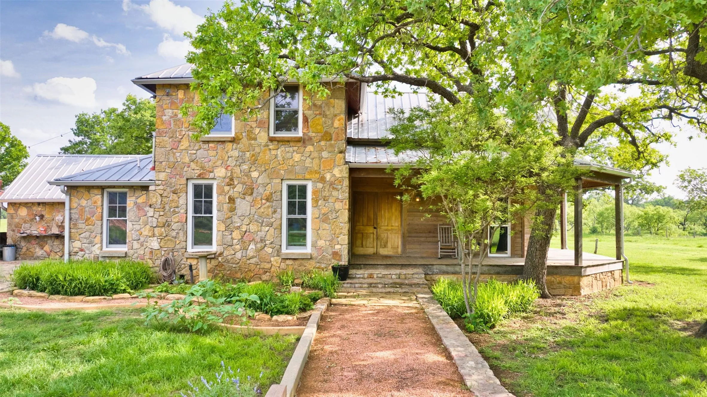 Stone-clad residence featuring a metal roof and a covered front porch with supporting columns