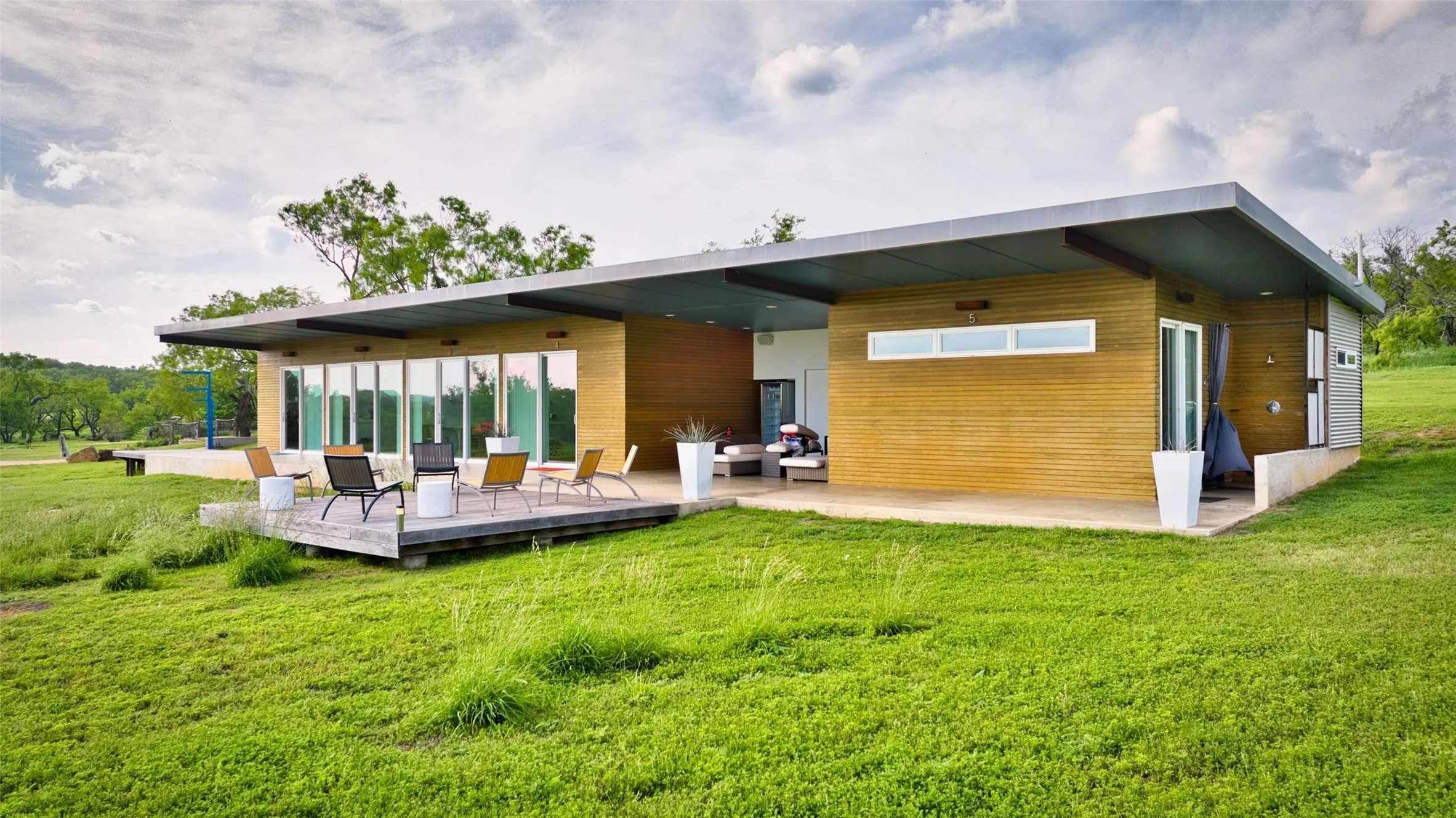 Modern single-story residence featuring a flat roofline with deep overhangs, extensive wood-panel siding, a concrete foundation, and a spacious outdoor deck