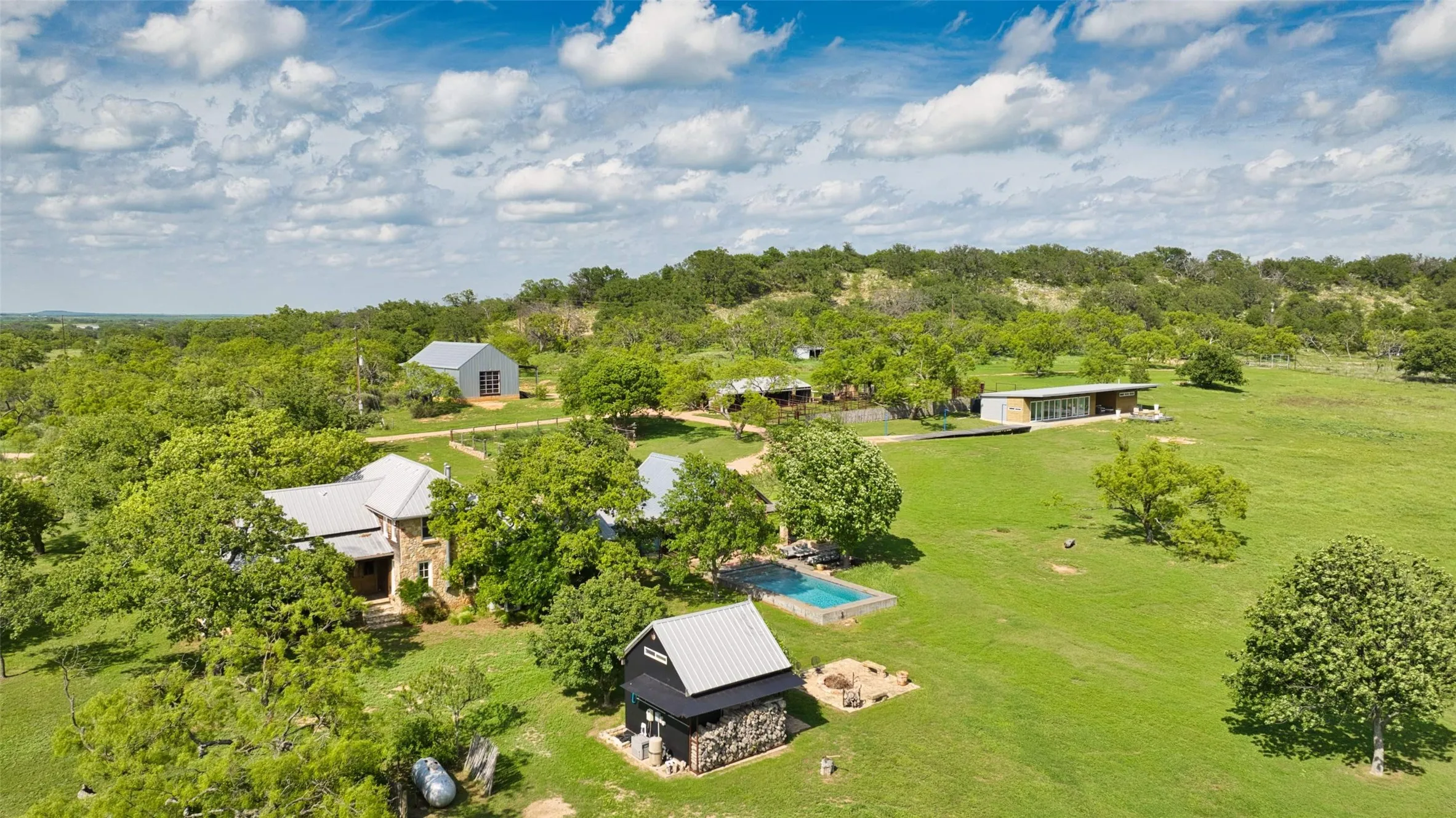 Expansive property featuring multiple structures, including a stone-clad residence with a metal roof and a modern-style building