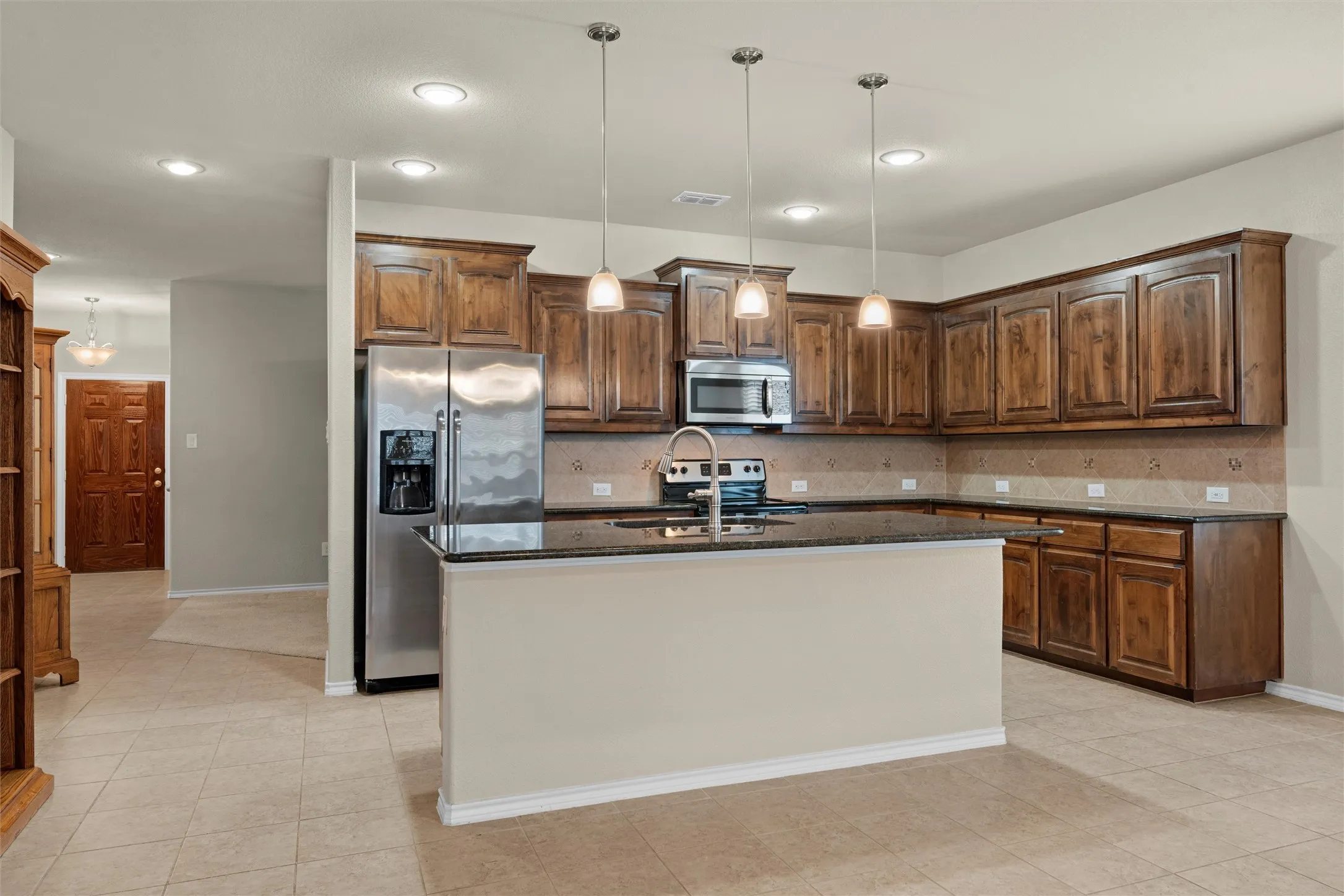 Kitchen featuring hanging light fixtures, stainless steel appliances, dark stone counters, a kitchen island with sink, and backsplash