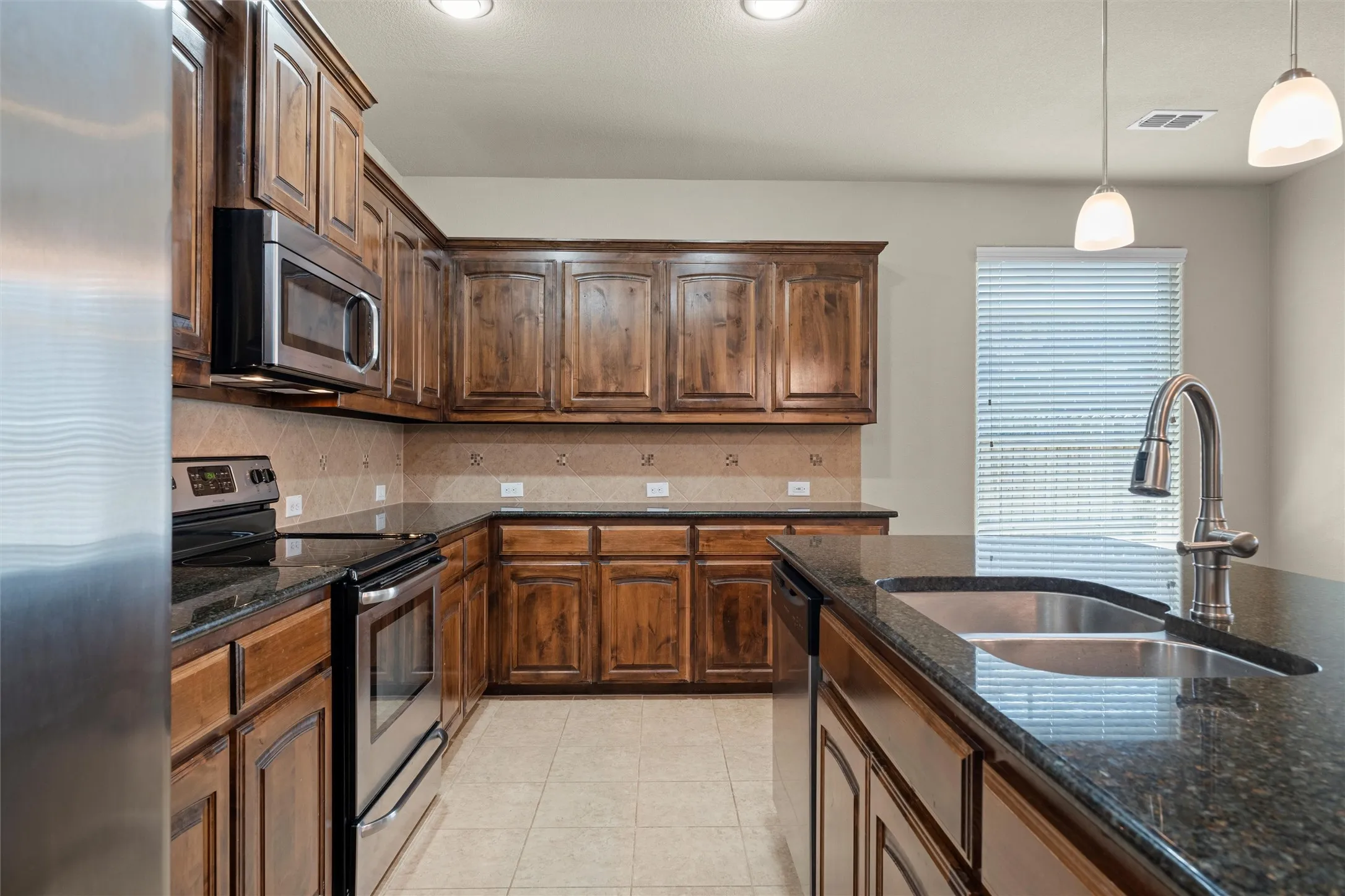 Kitchen featuring stainless steel appliances, dark stone countertops, decorative backsplash, hanging light fixtures, and recessed lighting