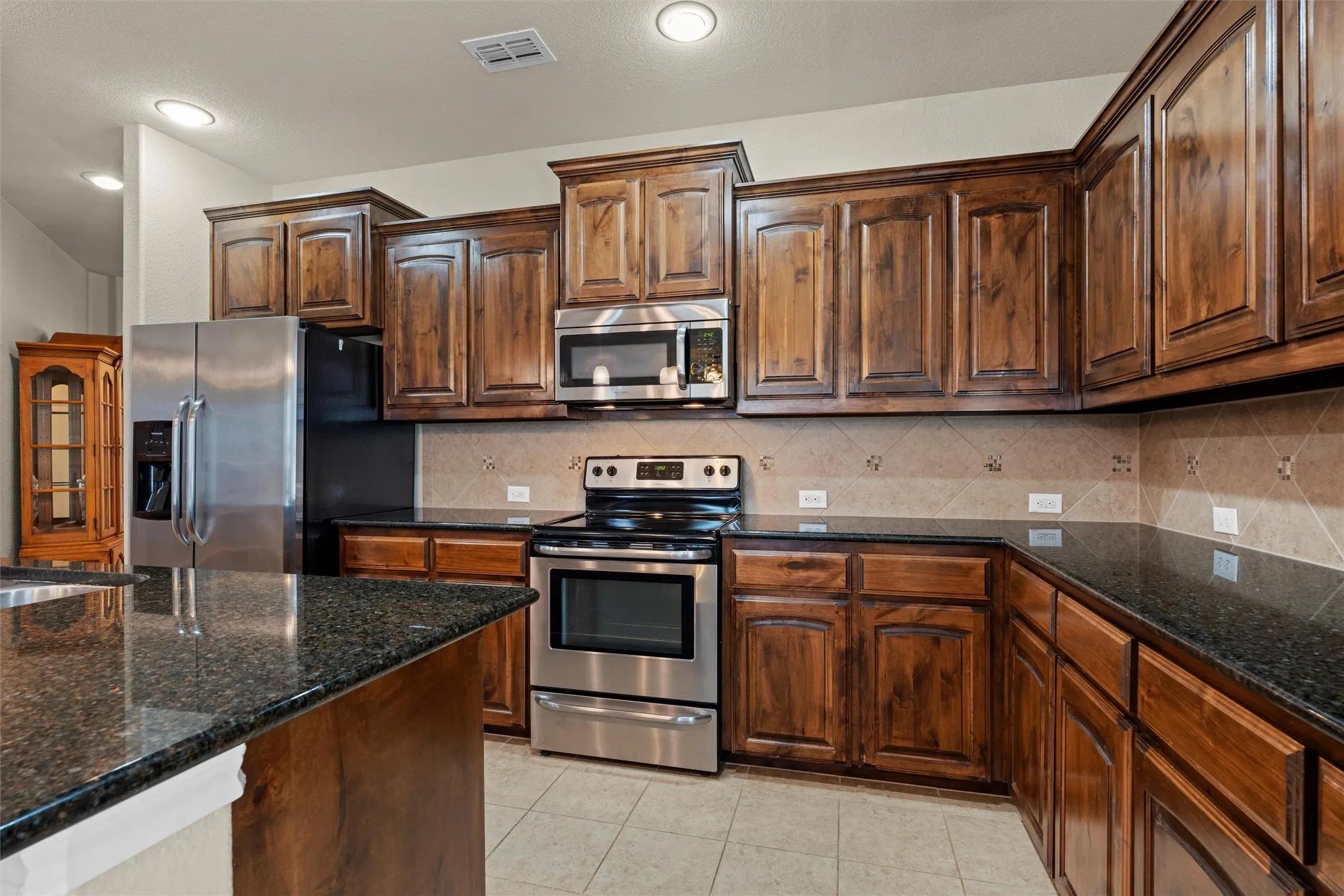 Kitchen featuring stainless steel appliances, dark stone counters, decorative backsplash, light tile patterned flooring, and recessed lighting