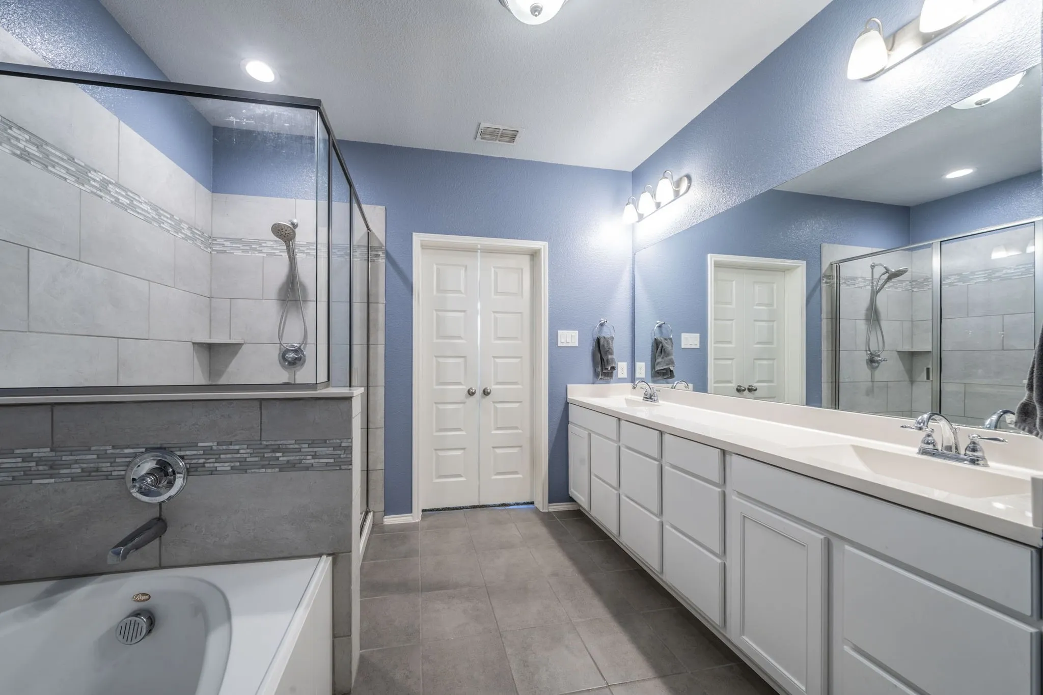 Full bath featuring double vanity, a bath, a shower stall, dark tile patterned floors, and recessed lighting