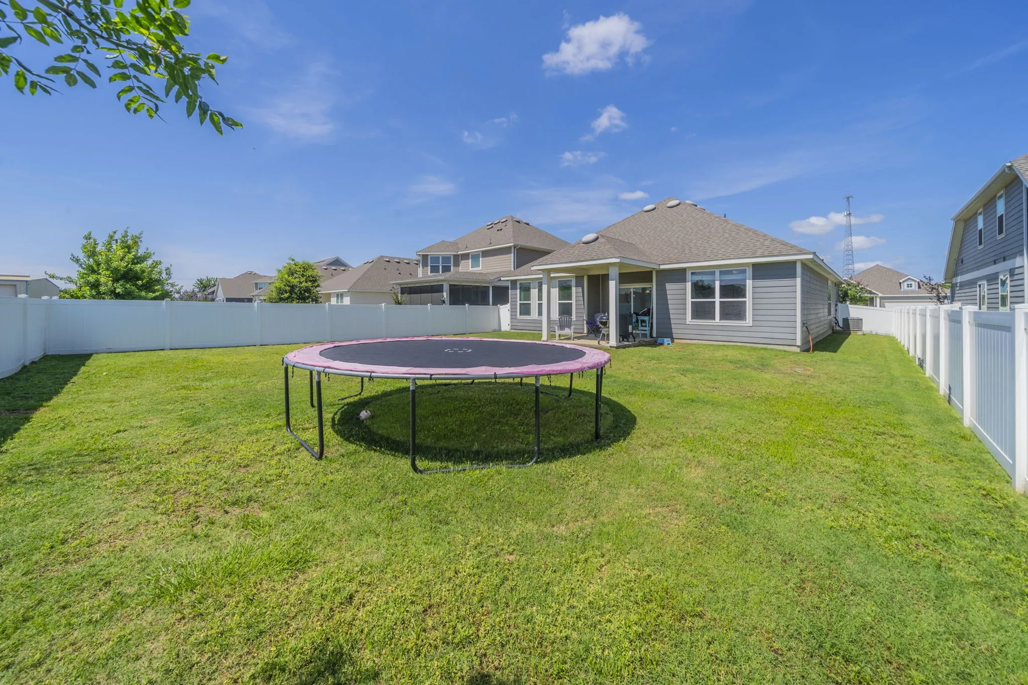 Rear view of house with a trampoline, a sunroom, and a fenced backyard
