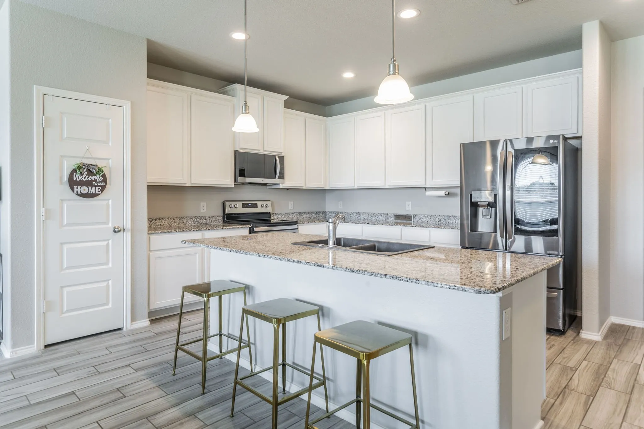 Kitchen with stainless steel appliances, light stone countertops, decorative light fixtures, wood finish floors, and white cabinets