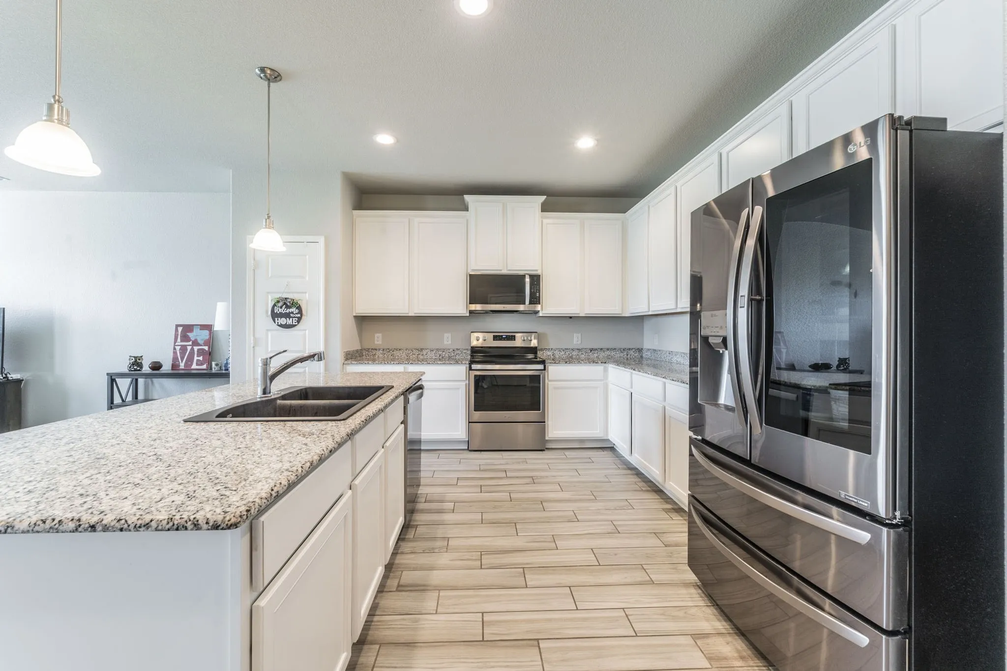 Kitchen with appliances with stainless steel finishes, white cabinetry, hanging light fixtures, an island with sink, and wood finish floors