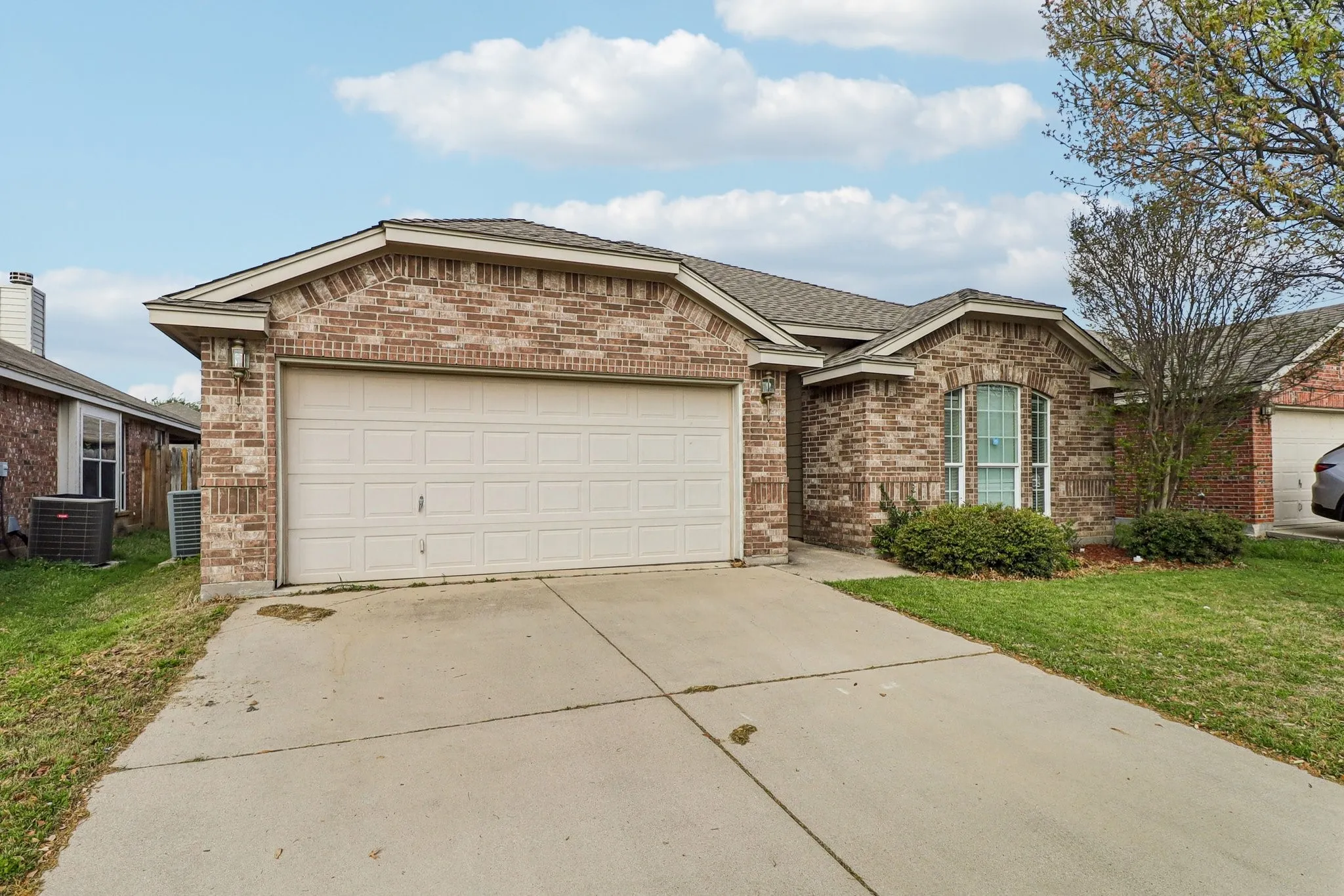 Ranch-style home with brick siding, an attached garage, concrete driveway, a front yard, and roof with shingles