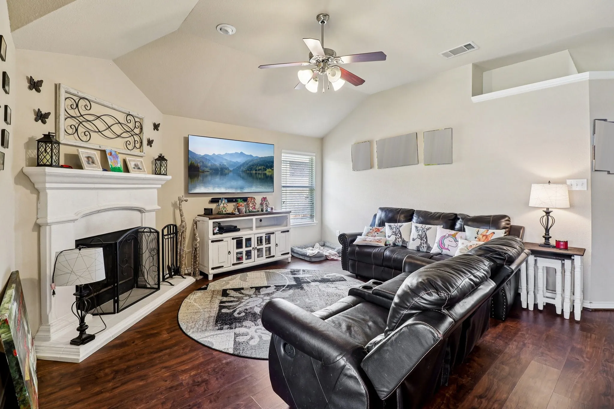 Living area with a ceiling fan, dark wood-style flooring, a fireplace with raised hearth, and vaulted ceiling