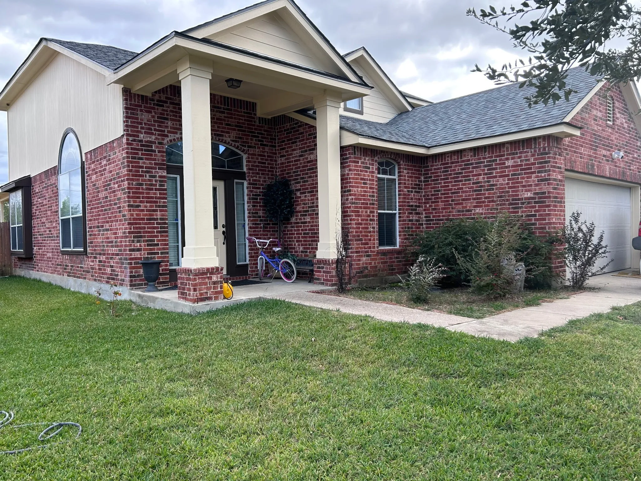 Entrance to property with brick siding, a shingled roof, a yard, and an attached garage
