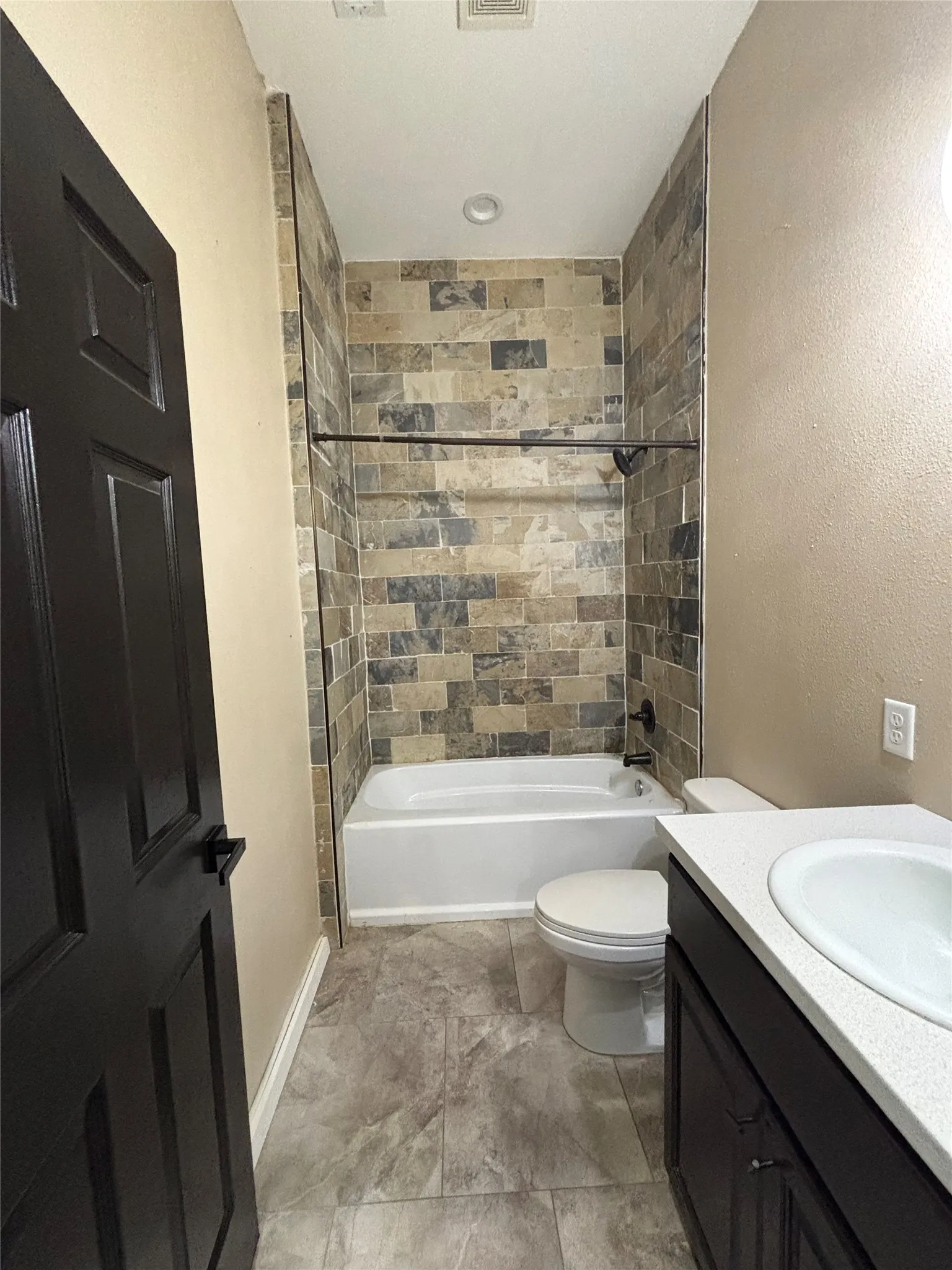 Bathroom featuring a tiled shower surround, white bathtub, and a dark wood-finish vanity with an integrated sink and light-toned countertop