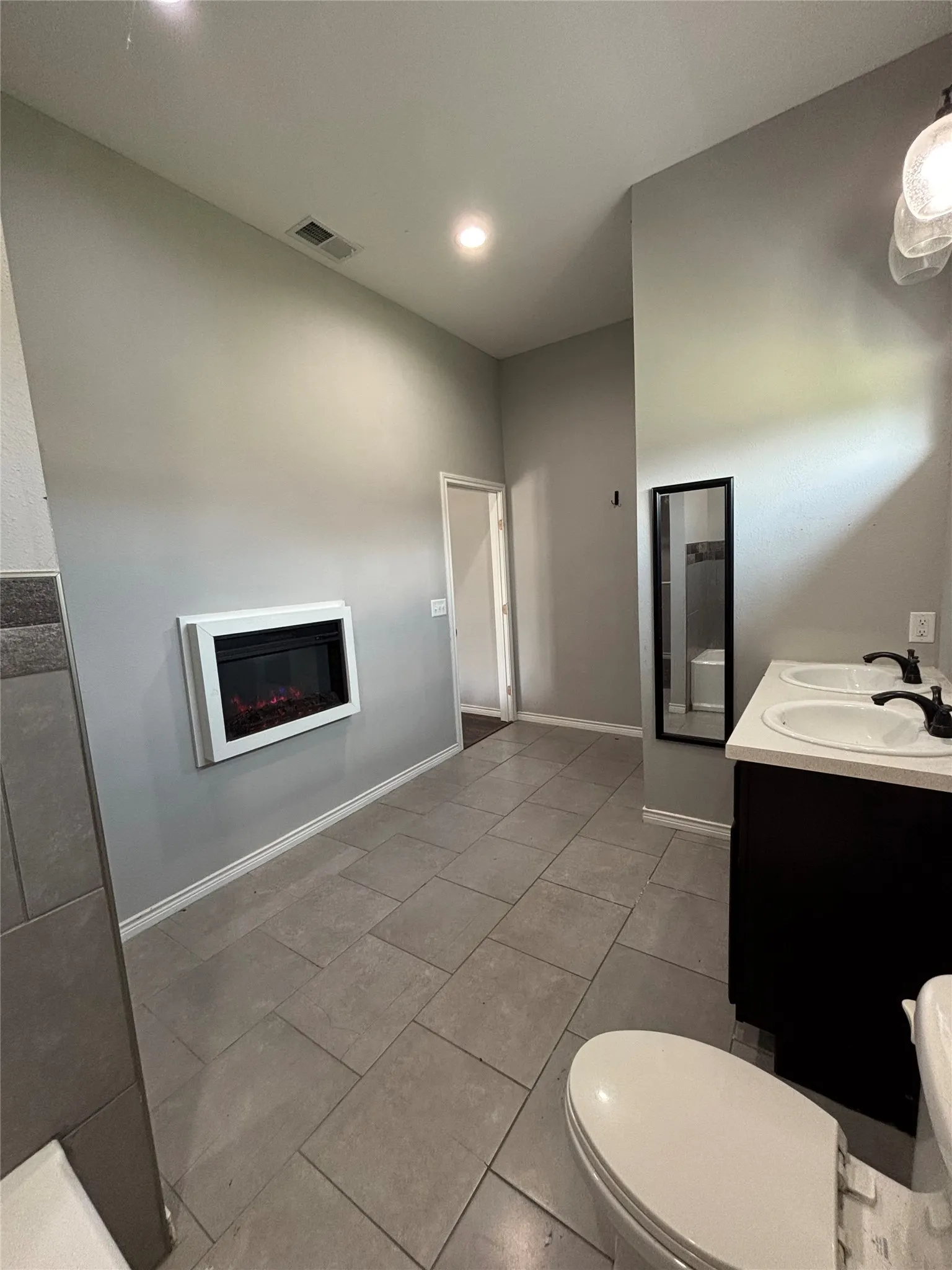 Spacious interior featuring a wall-mounted electric fireplace, tile flooring, dual basin vanity, and recessed lighting