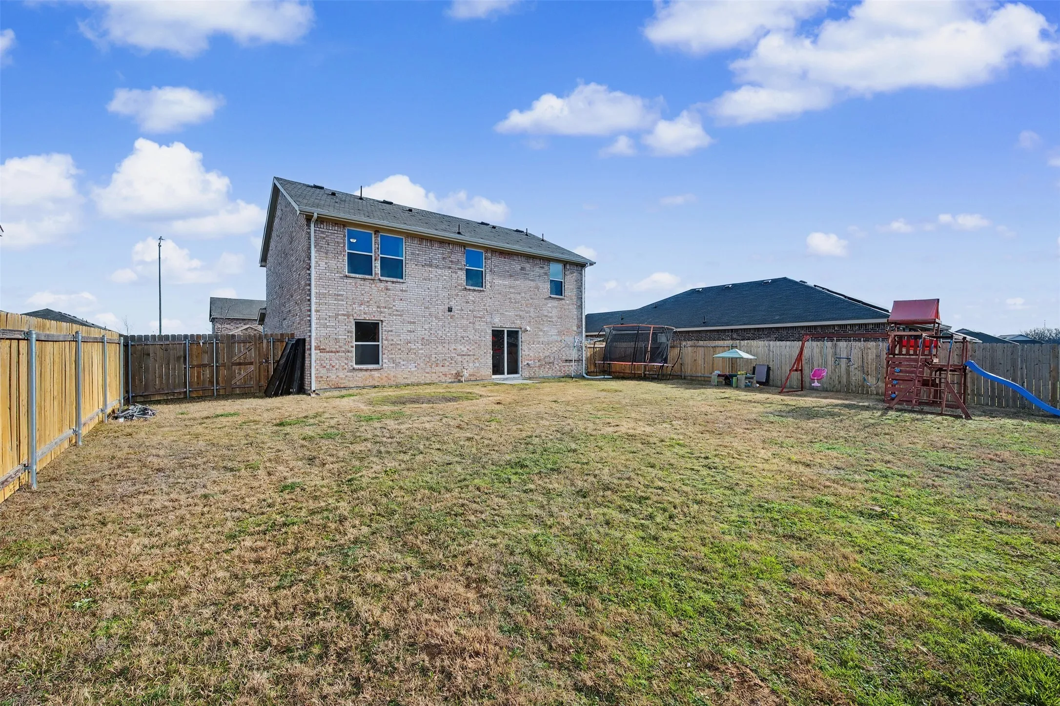 Back of property with a fenced backyard, brick siding, and a playground