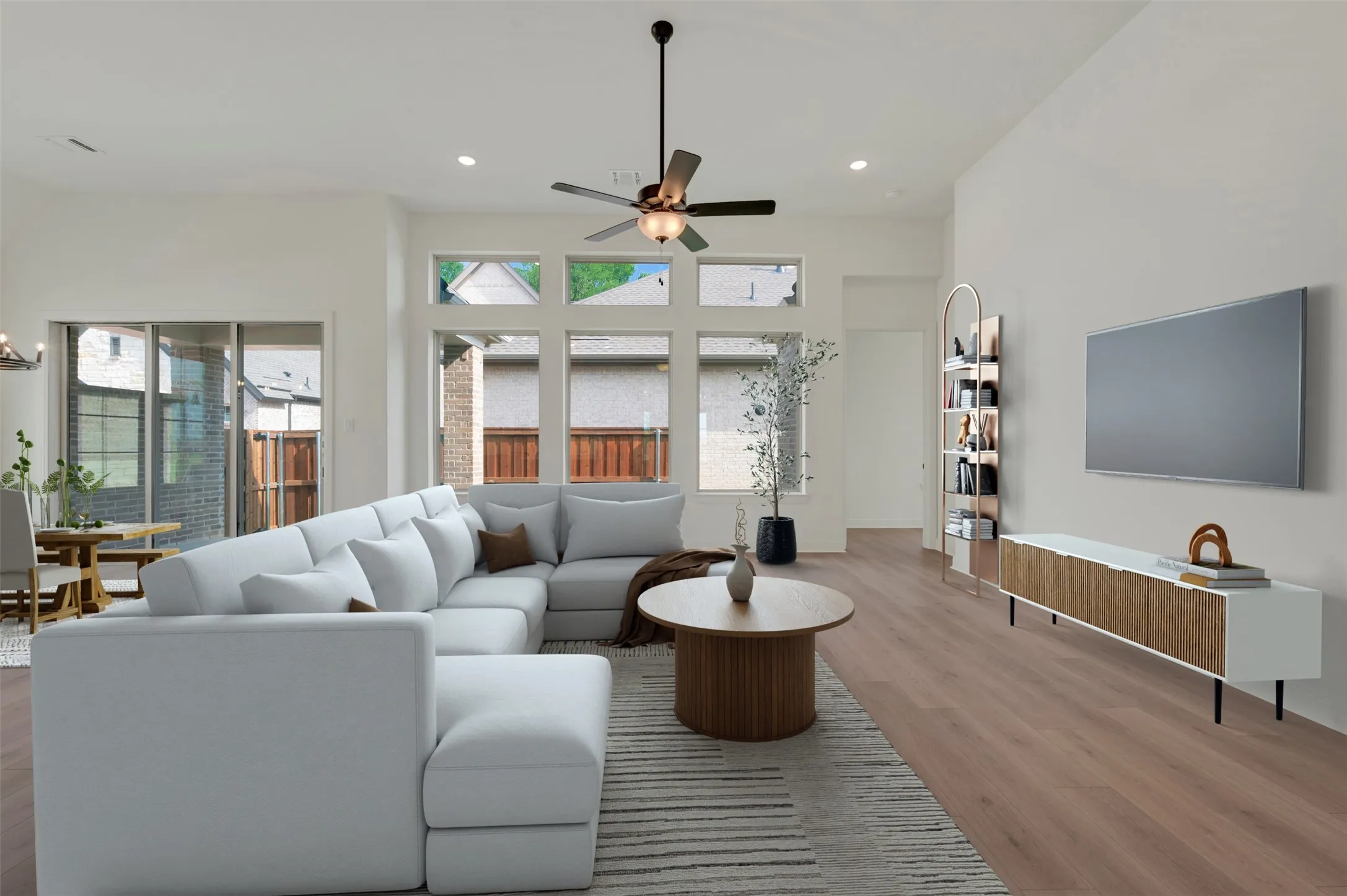 Spacious living area featuring wood-finish flooring, vaulted ceilings, and a ceiling fan with integrated lighting