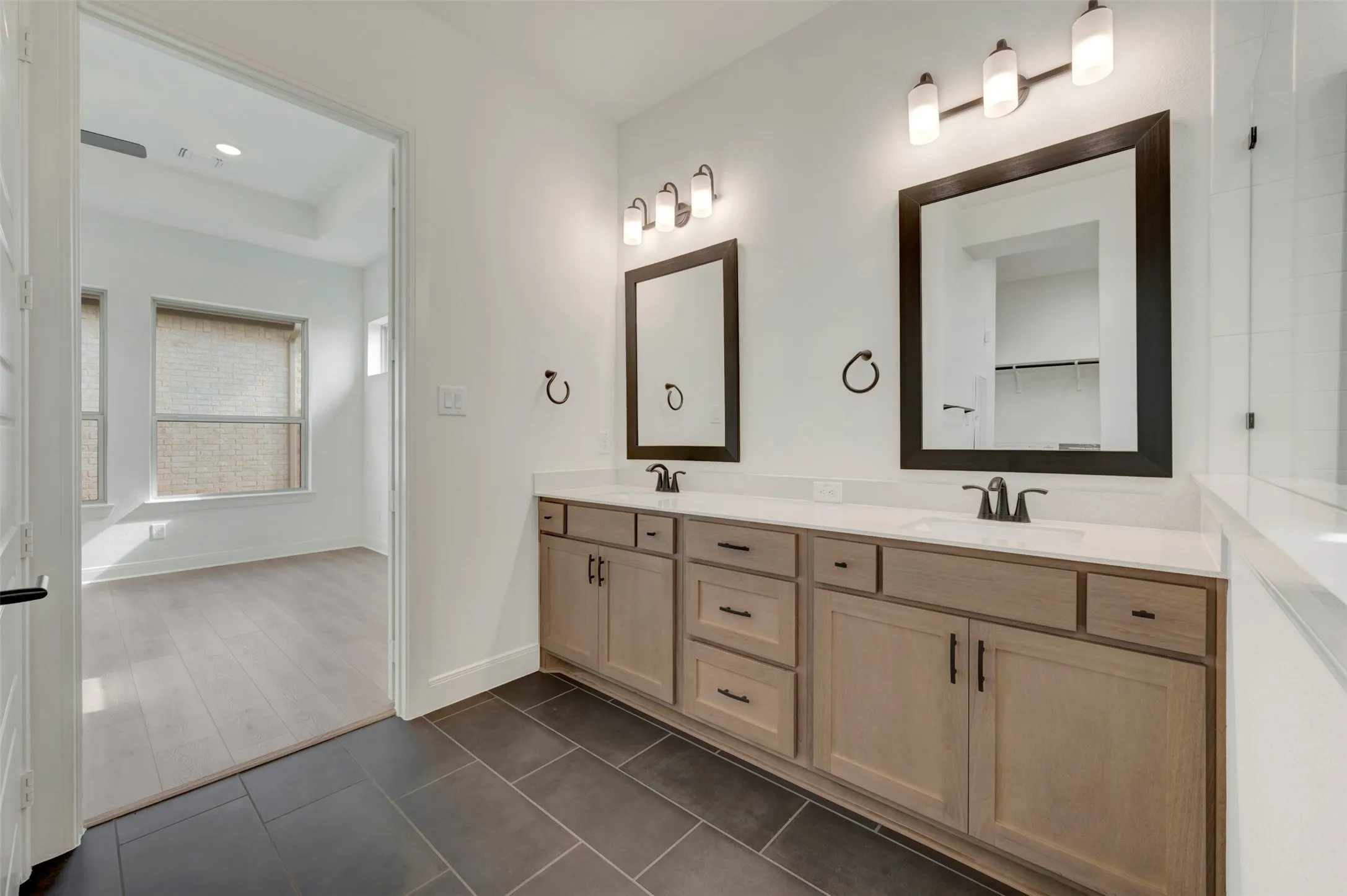 Double vanity with light wood-finish cabinetry, white countertops, and dual framed mirrors