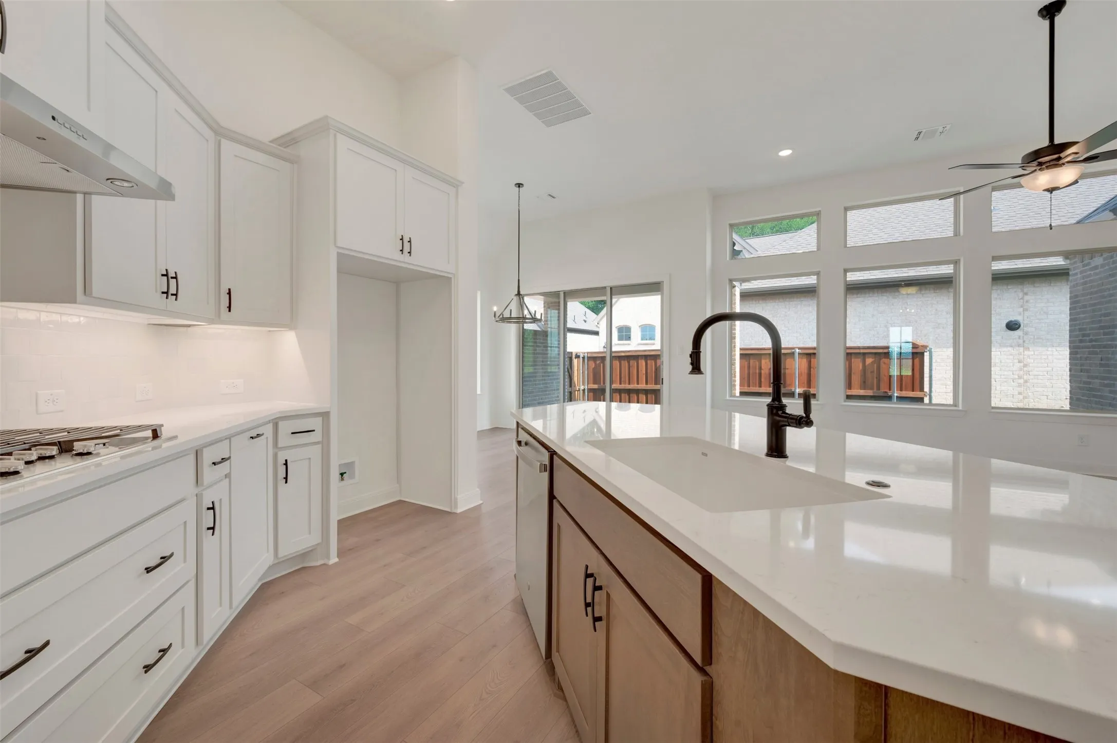 Open-concept kitchen featuring an oversized island with an undermount sink, white shaker cabinetry with dark hardware, a gas cooktop, and wood-finish flooring