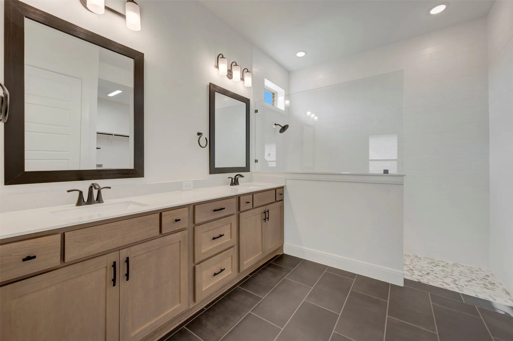 Bathroom featuring a dual vanity with light wood-finish cabinetry, white countertops, and dark framed mirrors