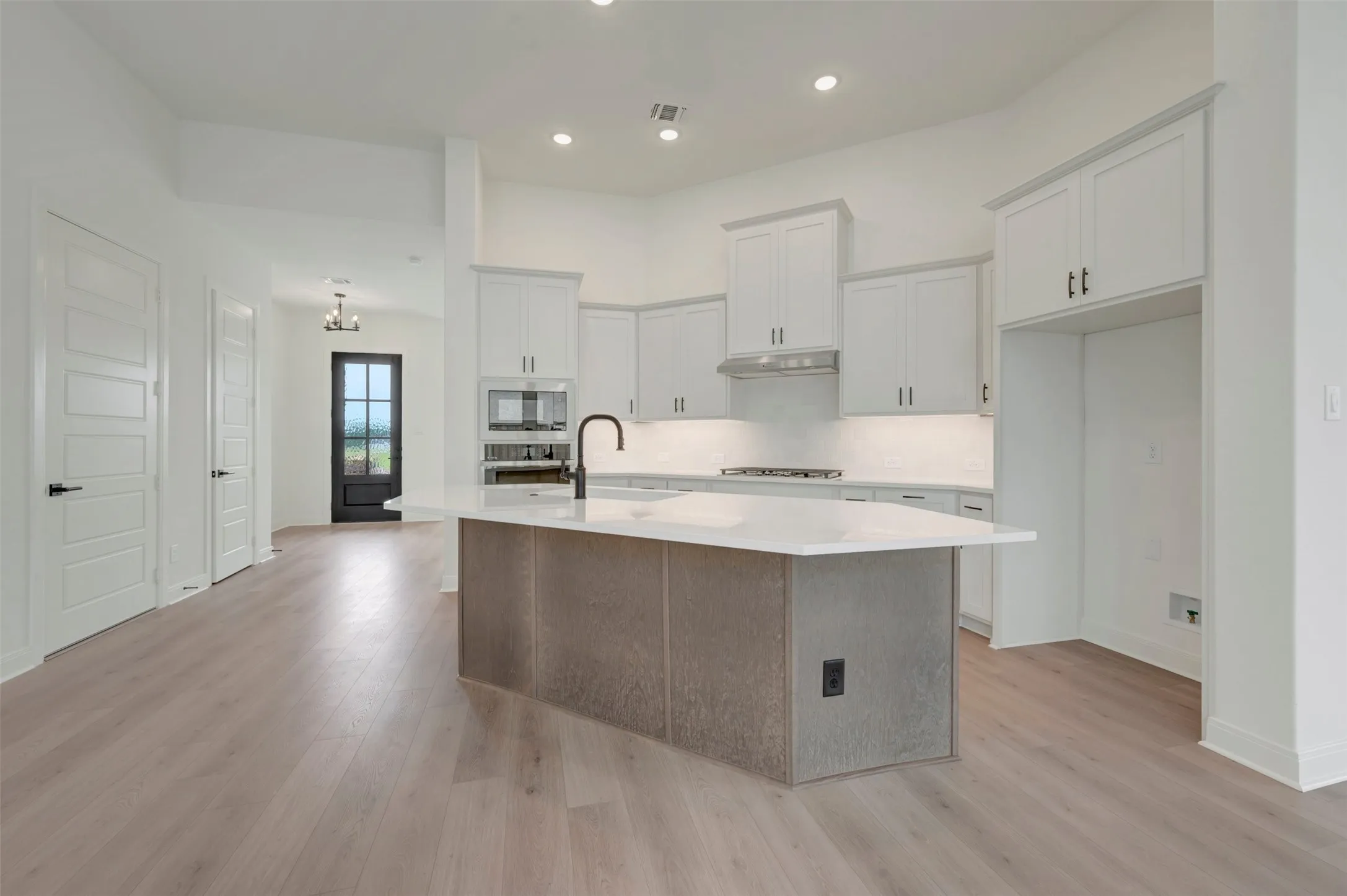 Modern kitchen featuring an expansive island with a light-toned countertop, white cabinetry, integrated microwave, and wood-finish flooring