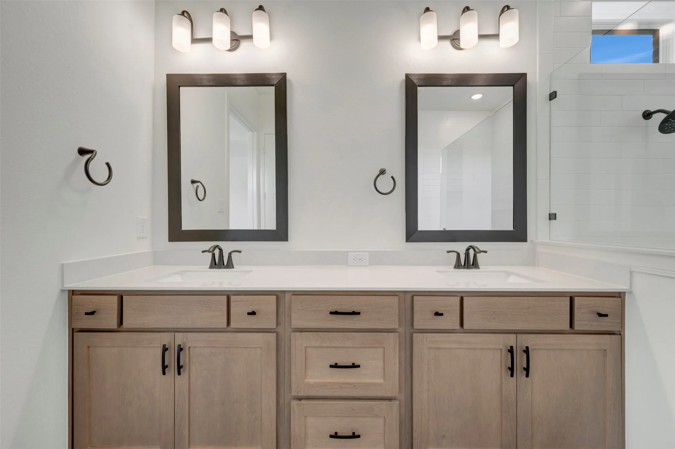 Dual vanities featuring light wood-finish cabinetry, white countertops, and black hardware