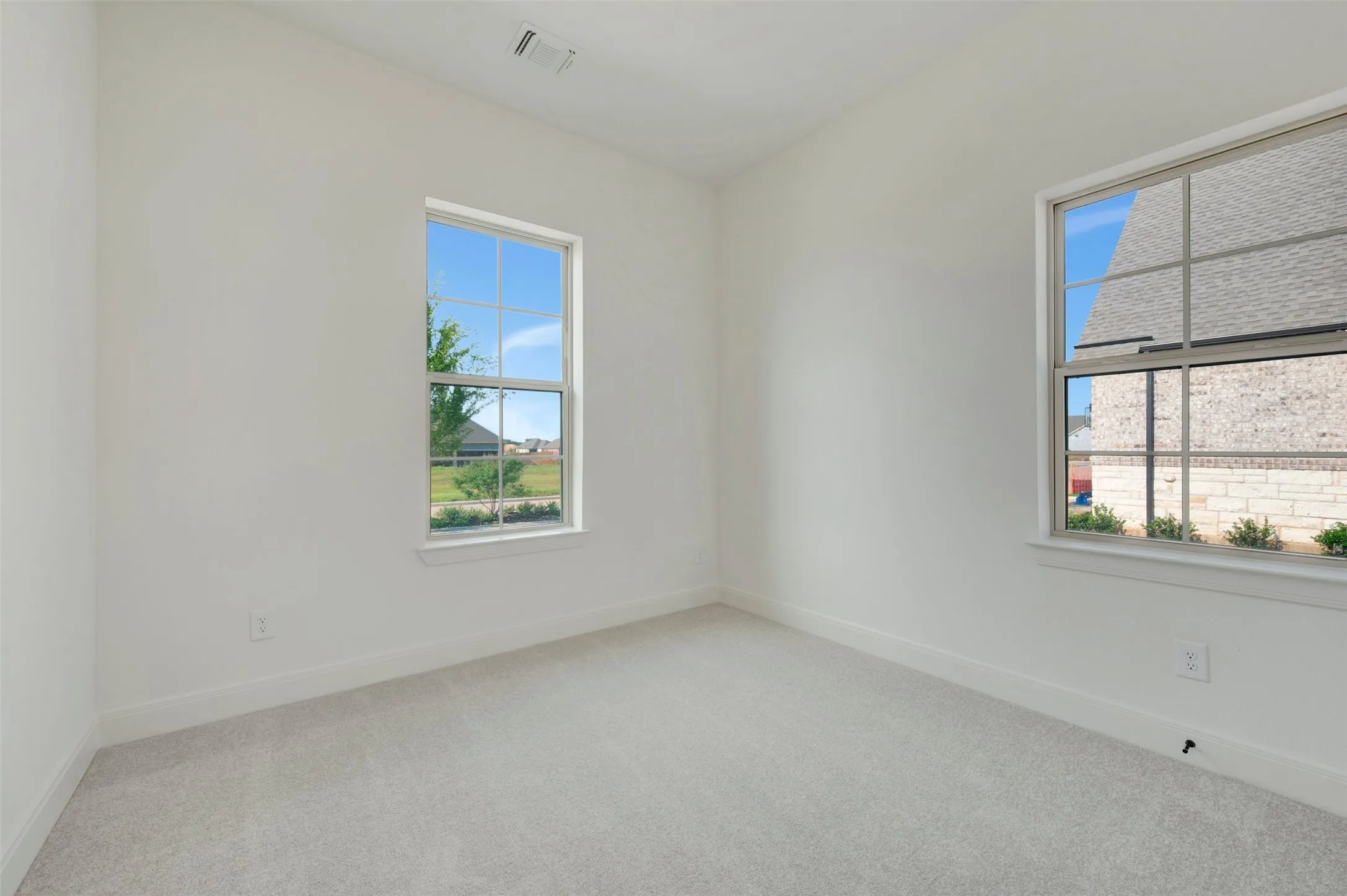 Spacious room featuring two large windows with grid patterns, light-colored carpeting, white baseboards, and a neutral wall palette