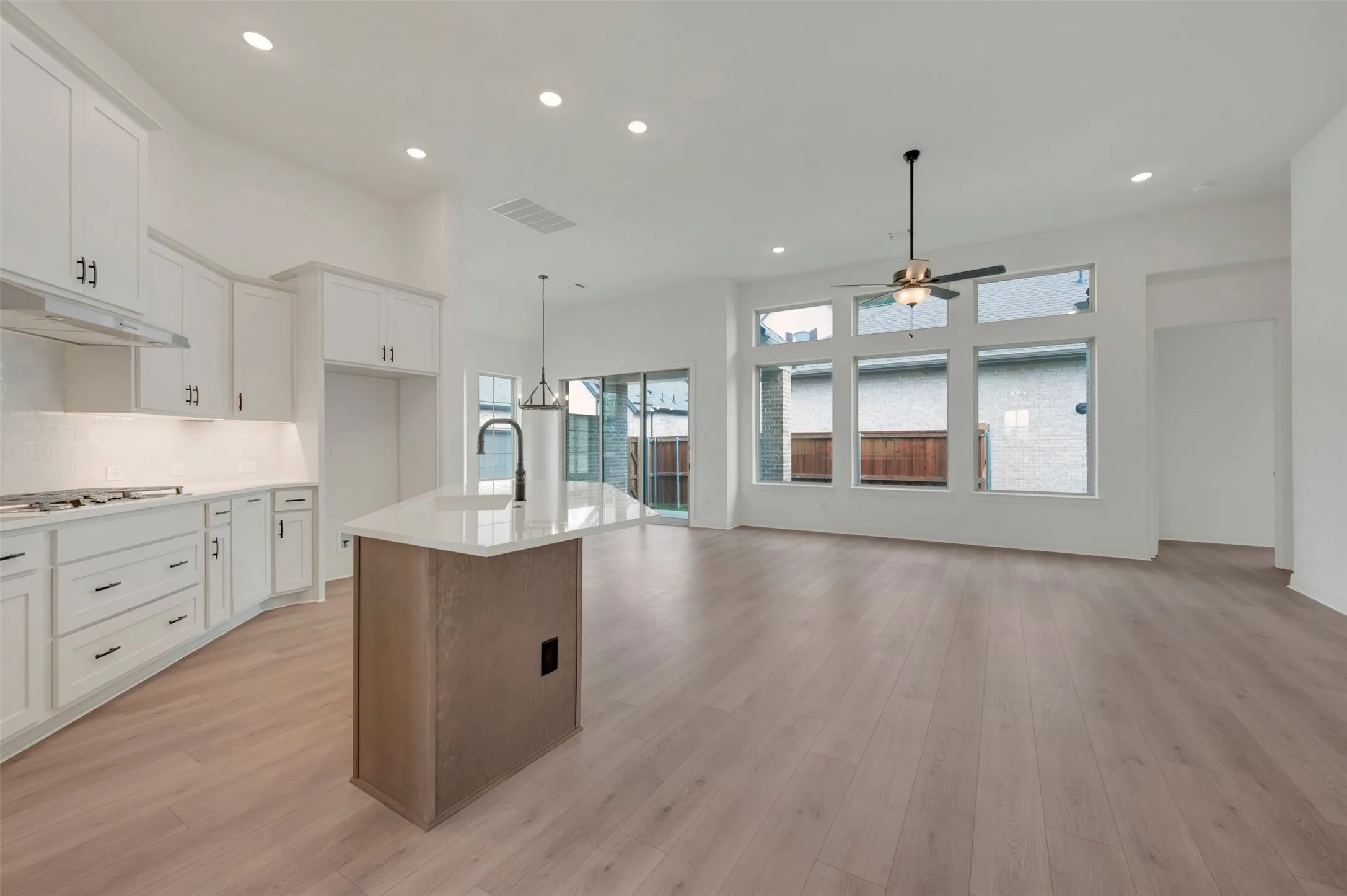 Open-concept living space featuring wood-finish flooring, a contemporary kitchen island with a quartz countertop, white cabinetry with dark hardware, recessed lighting, and a wall of windows