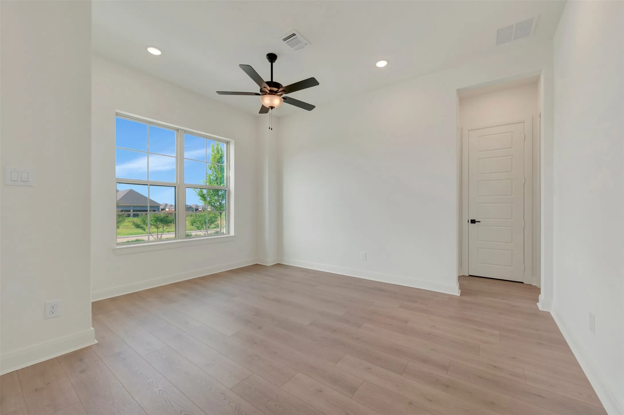 Spacious room featuring wood-finish flooring, a multi-pane window, and a ceiling fan with integrated lighting