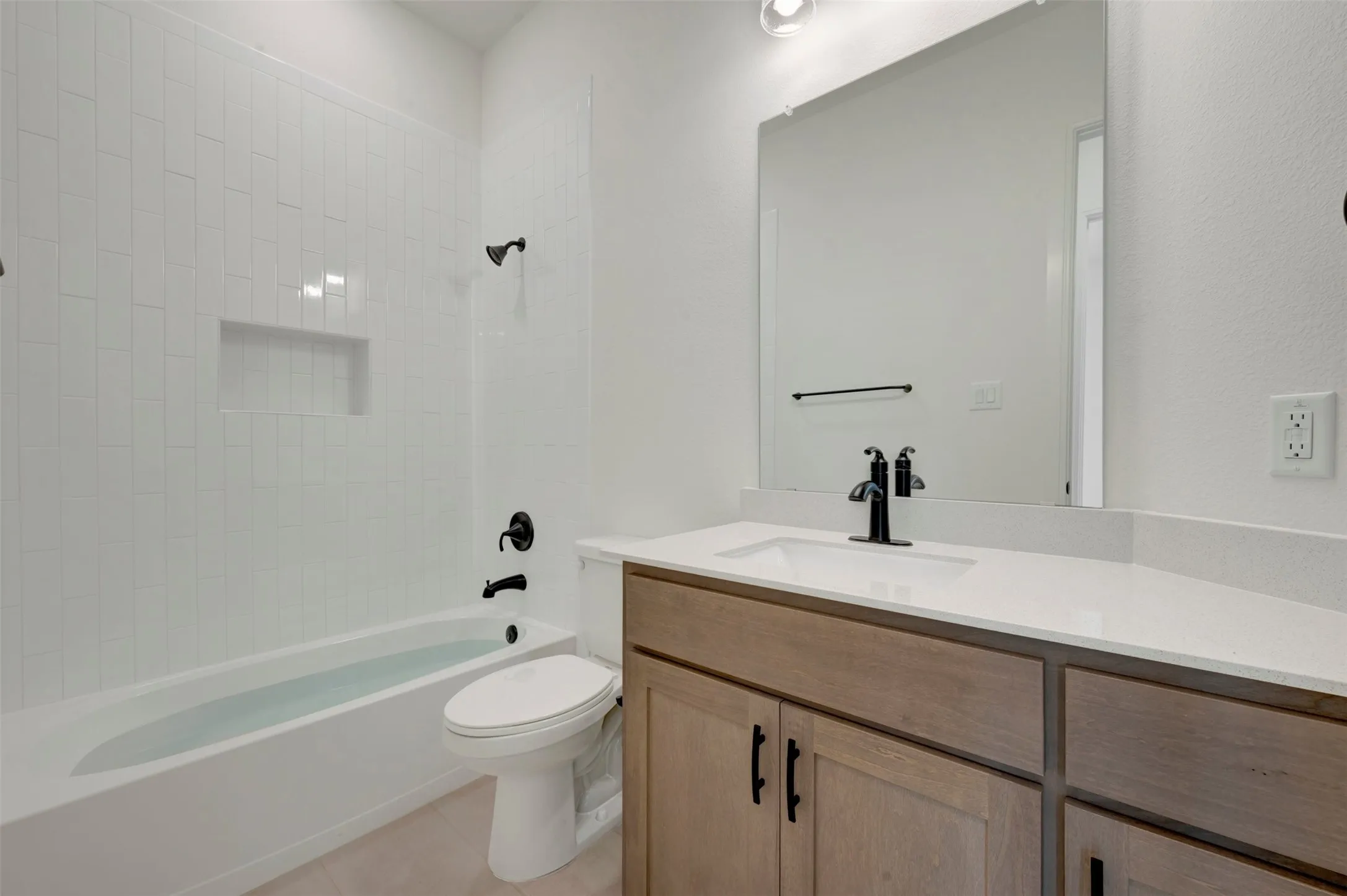 Bathroom featuring a spacious tub with white subway tile surround, integrated shower niche, and matte black fixtures