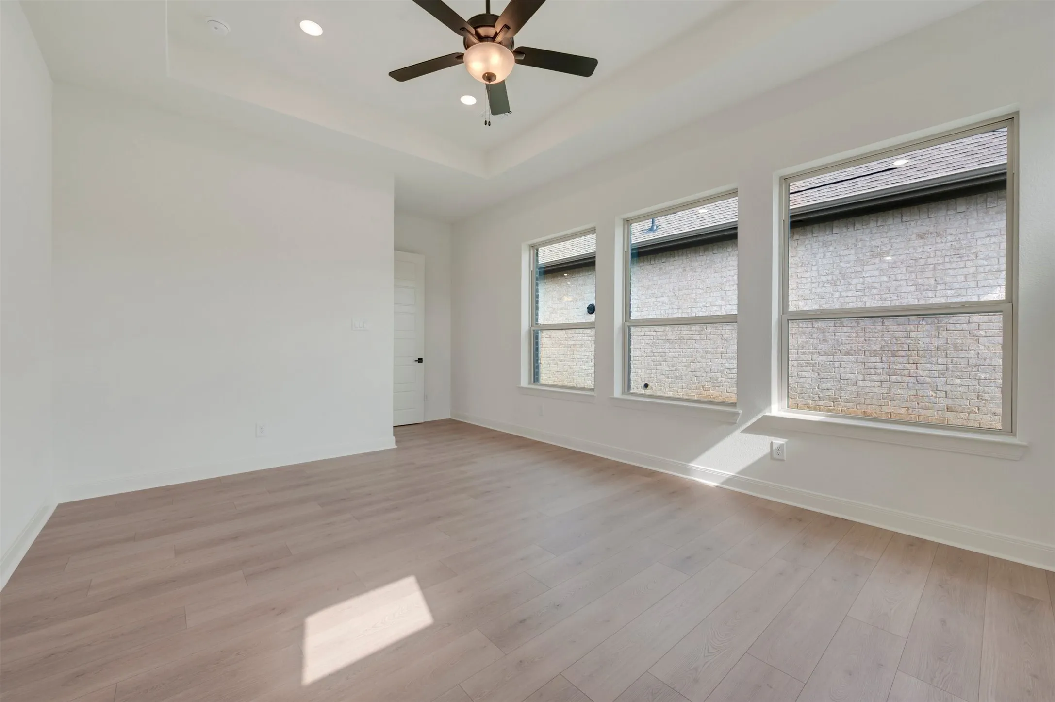 Spacious room featuring wood-finish flooring, a tray ceiling, and recessed lighting