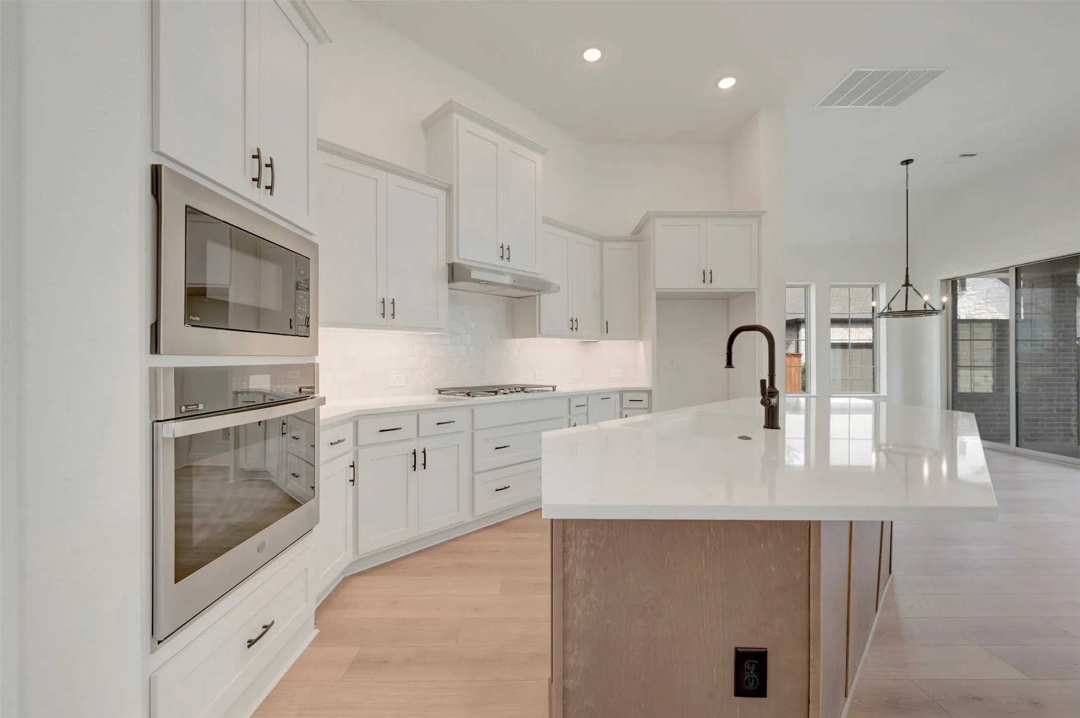 Modern kitchen featuring white cabinetry, light countertops, stainless steel appliances including a built-in microwave and oven, and wood-finish flooring