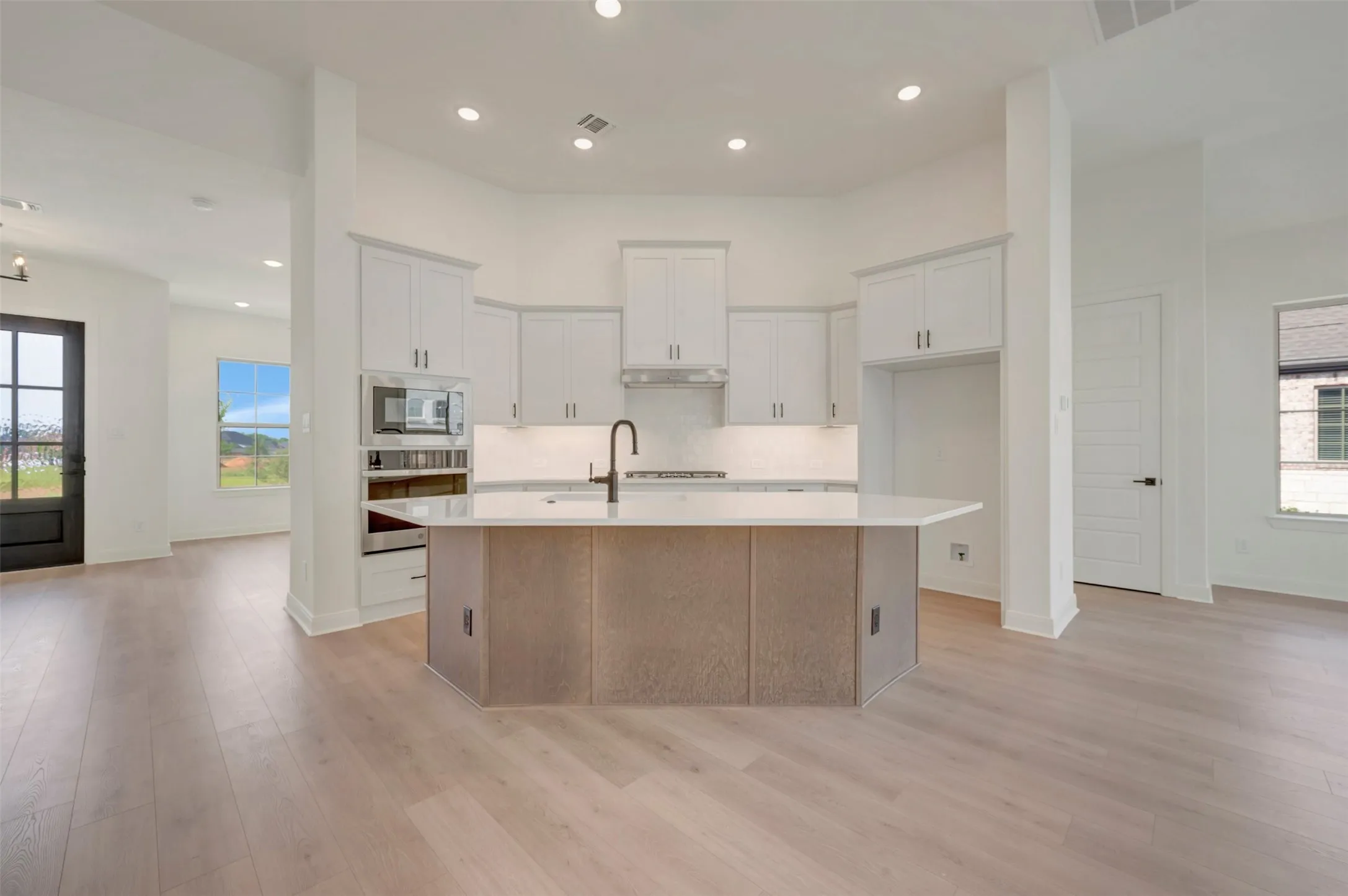 Spacious kitchen featuring a central island with a light-toned wood-finish base and light-colored countertop, white cabinetry, built-in microwave, and wood-finish flooring