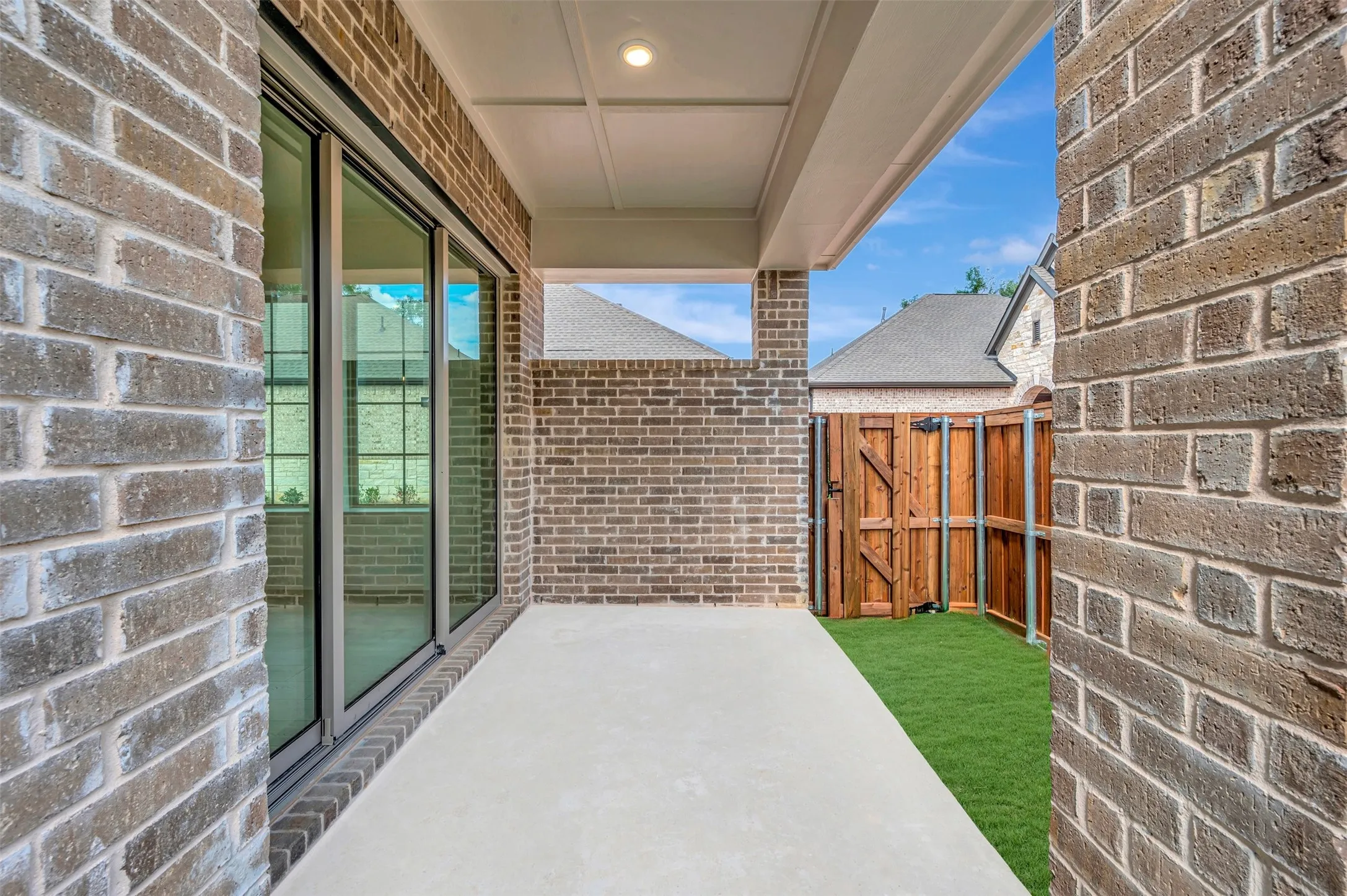 Covered patio with a concrete surface, featuring brick exterior walls and a recessed ceiling light