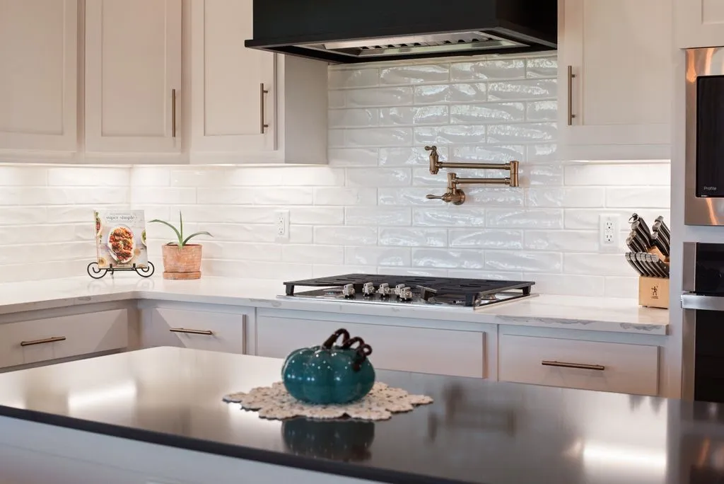 White shaker-style cabinetry, white subway tile backsplash, white countertops, built-in gas range, and a pot filler faucet