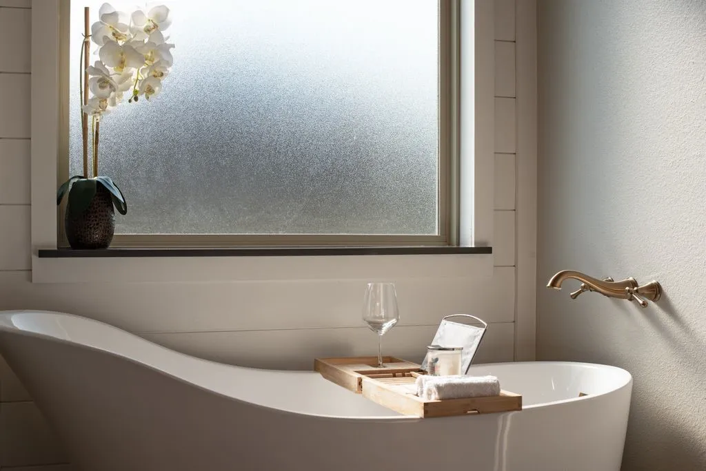 Freestanding soaking tub with wall-mounted brass-finish faucet, frosted window, and shiplap-style wall paneling