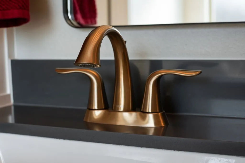 Bronze-tone two-handle widespread faucet set on a dark countertop with an integrated backsplash