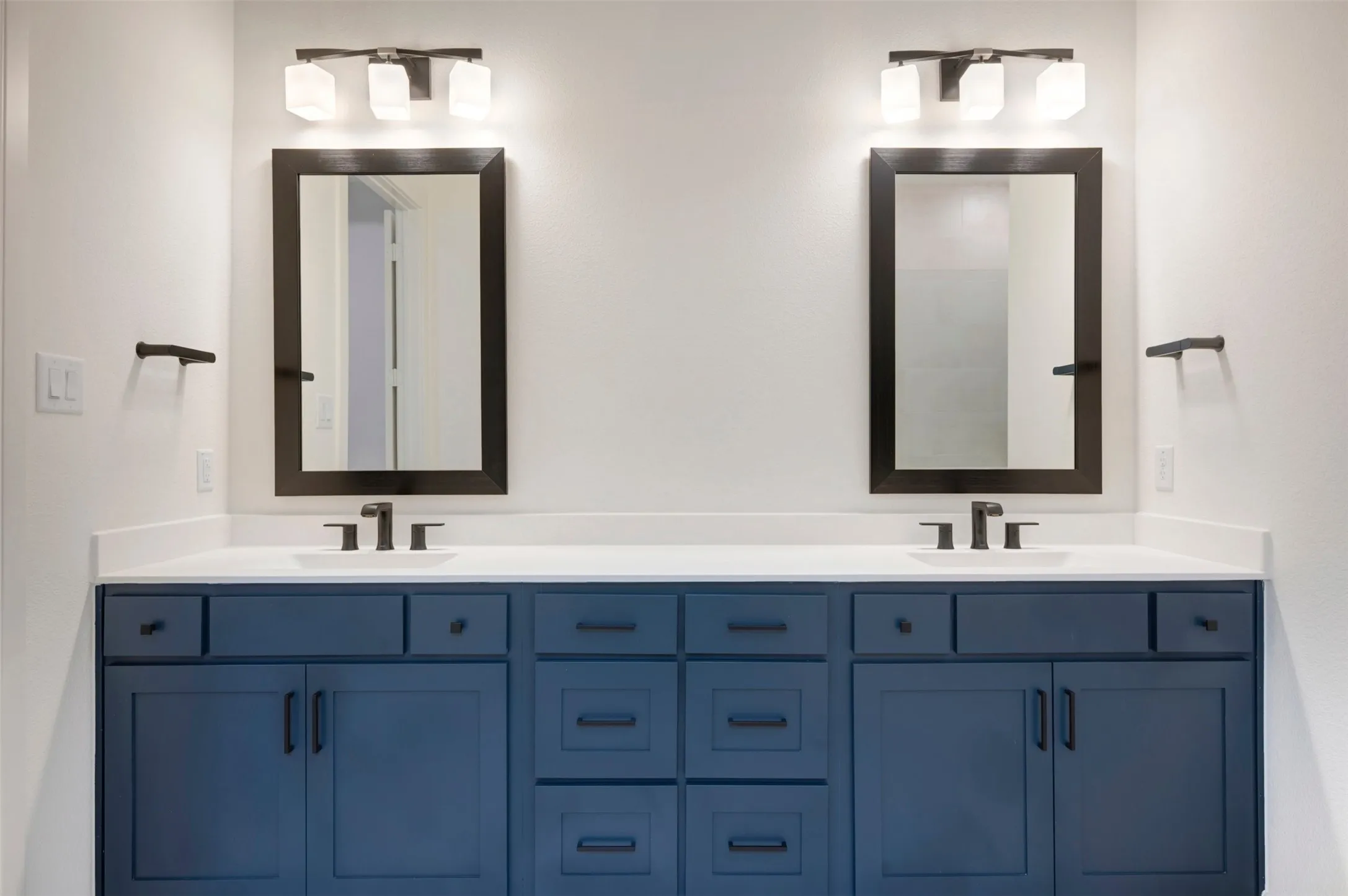 Bathroom featuring a dual vanity with navy blue cabinetry, white countertops, and contemporary black framed mirrors