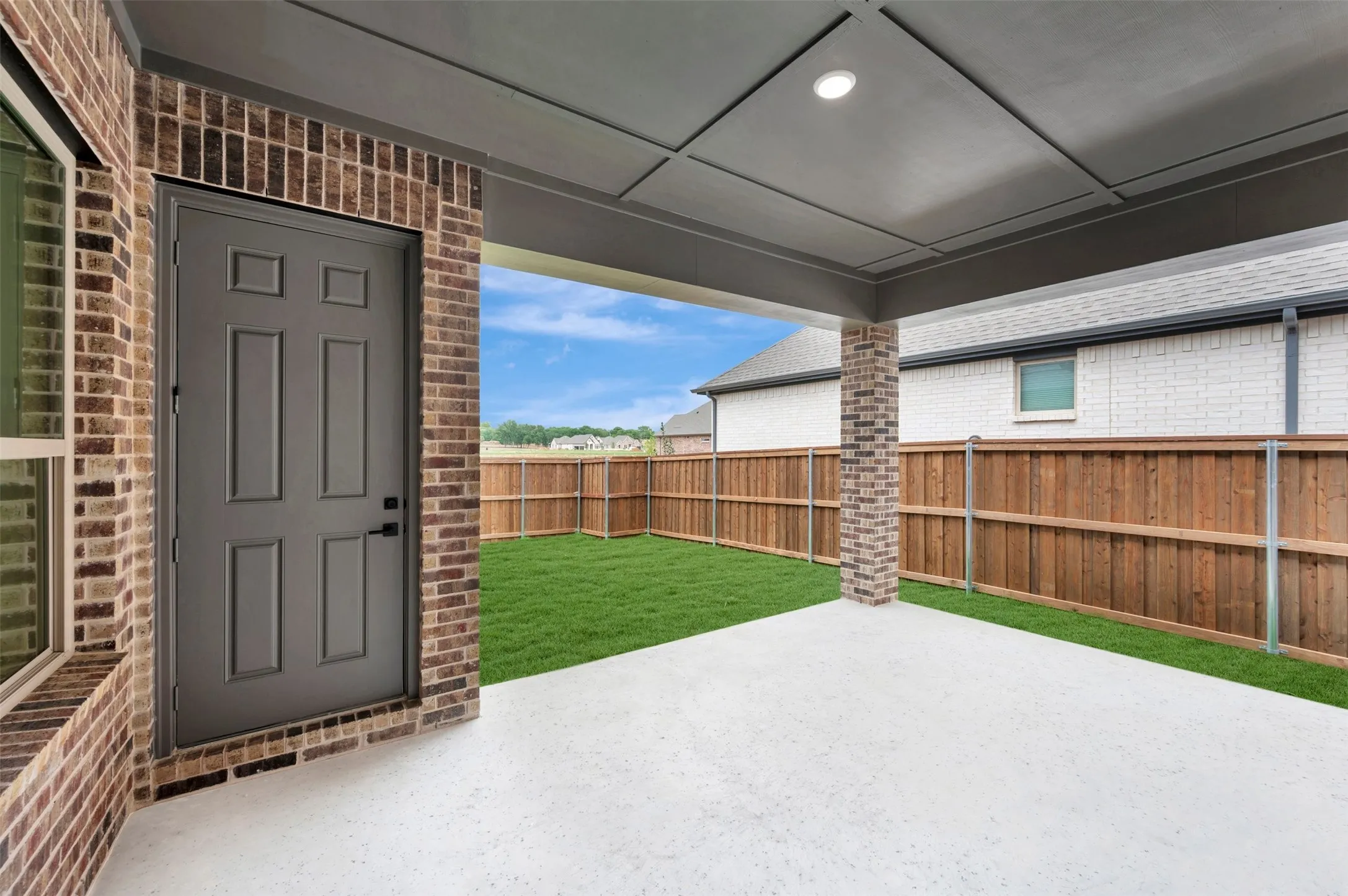 The property features a covered patio with a concrete floor, a brick support column, and a paneled ceiling with recessed lighting