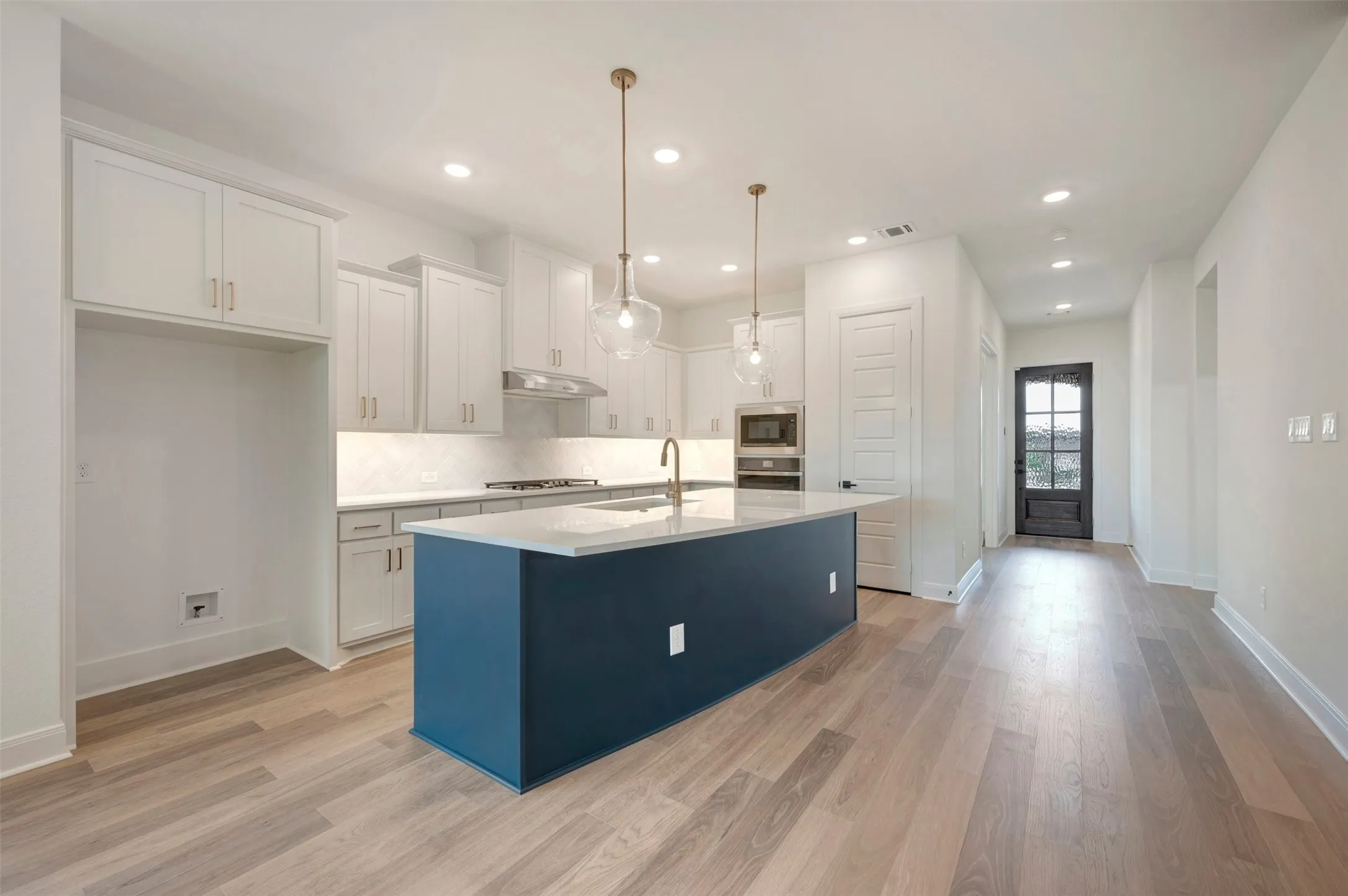 Modern kitchen featuring light wood flooring, white cabinetry, and a contrasting blue kitchen island with a white countertop