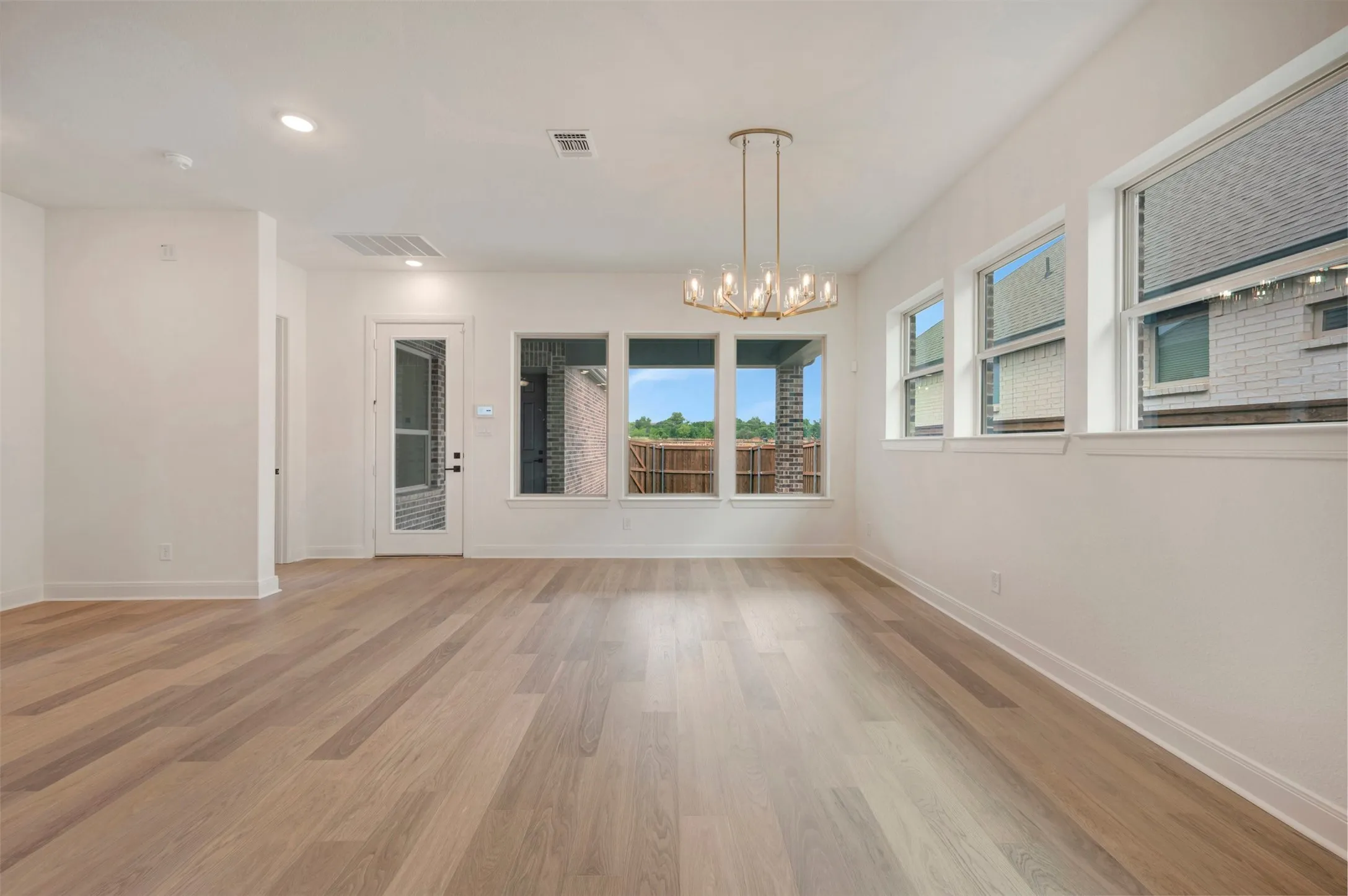 Spacious room featuring light-colored hardwood floors, white walls, and a modern chandelier